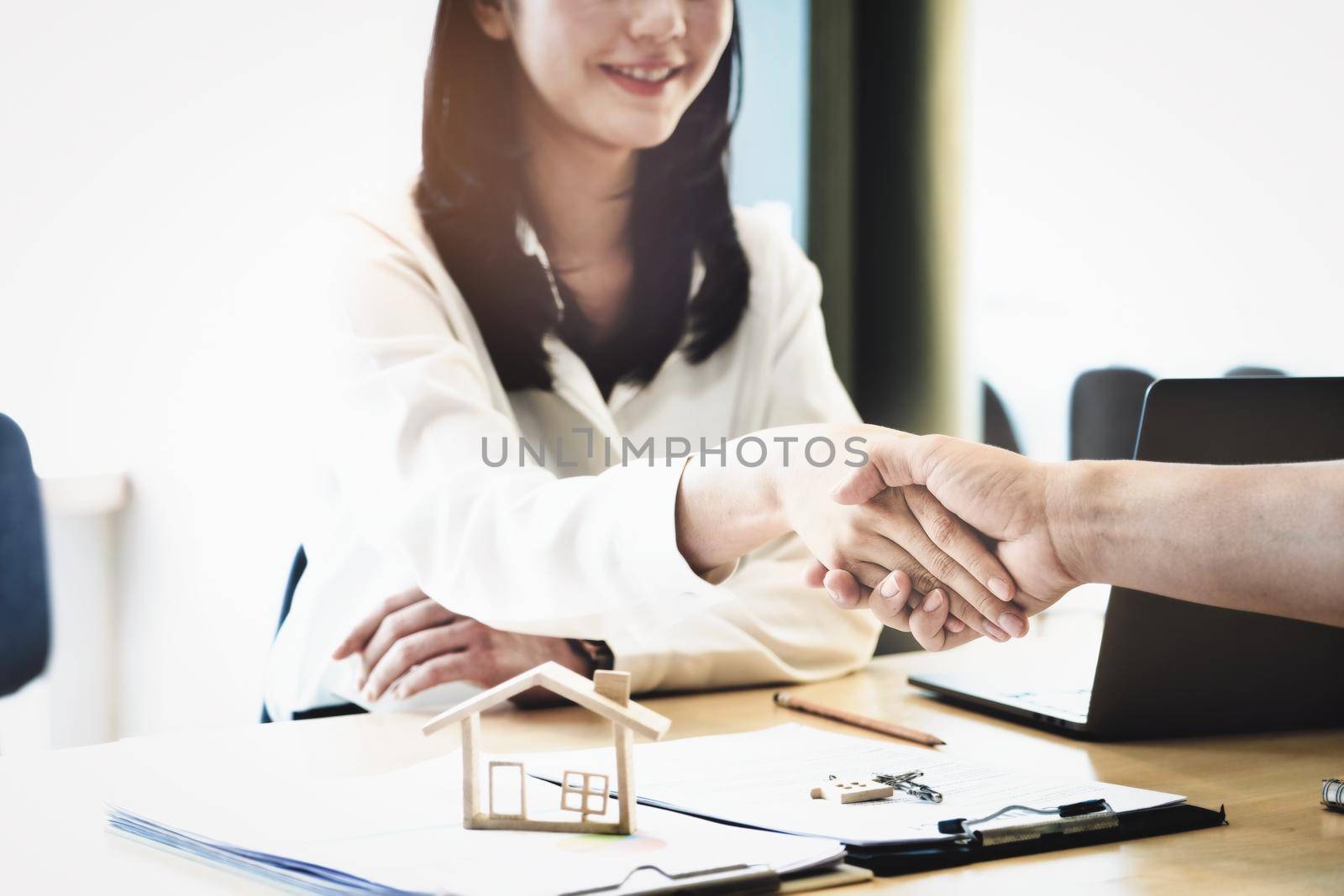 Focus on the congratulatory handshake. The real estate agent agrees to buy the home to the customer at the agent's office. conceptual agreement by Manastrong