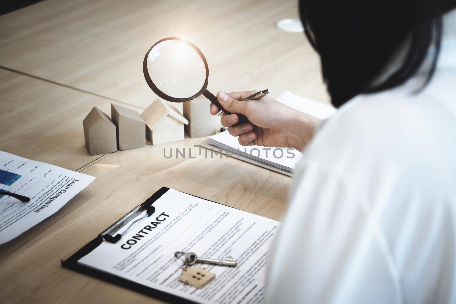 Inspector Concept, a customer is holding a magnifying glass to look at each house model to check the price of a home loan for each model