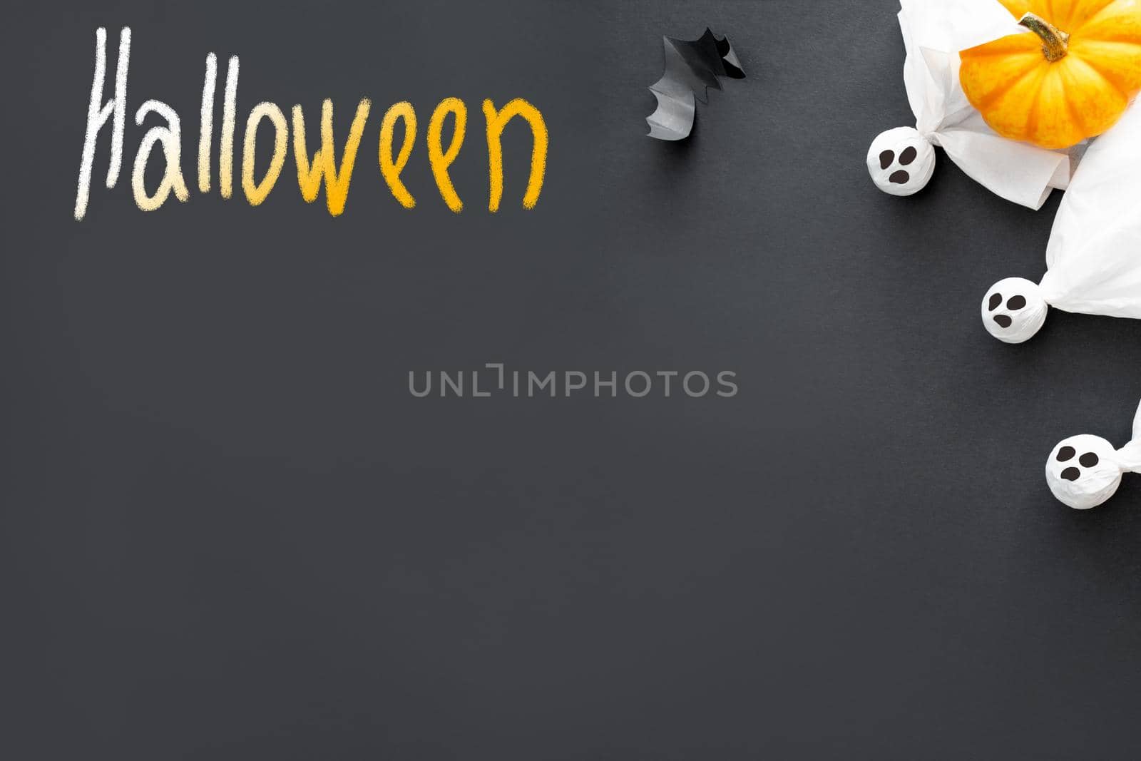 Three ghosts, pumpkin, bat and word halloween on black background, concept of Halloween. Postcard, copy space, flat lay