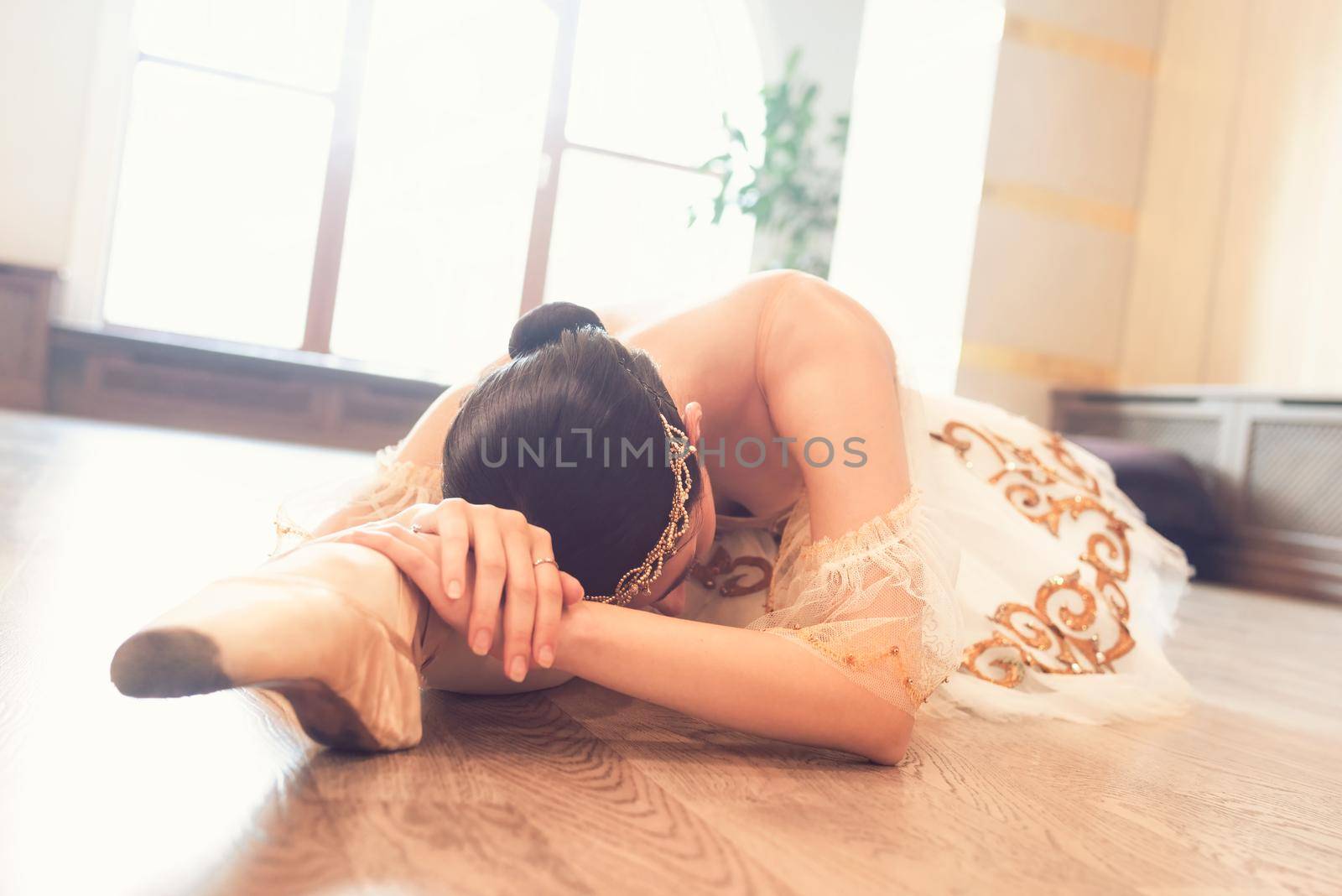 A ballerina in a white tutu warming up before training lying on the studio floor