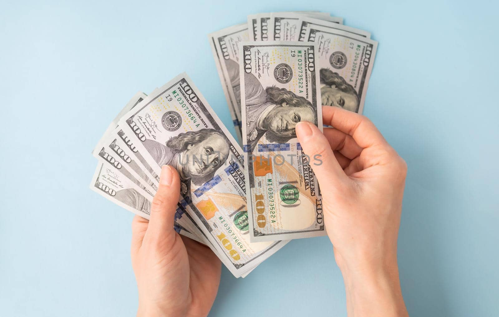 Female hands counting 100 dollar bills isolated on a blue background