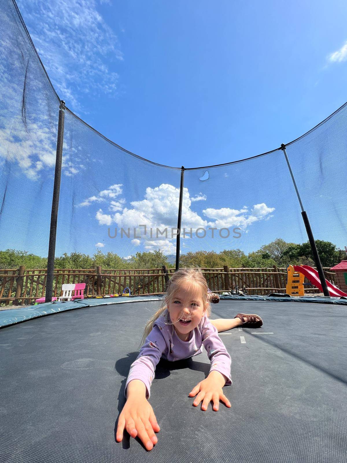 Smiling little girl lying on her stomach on a trampoline. High quality photo