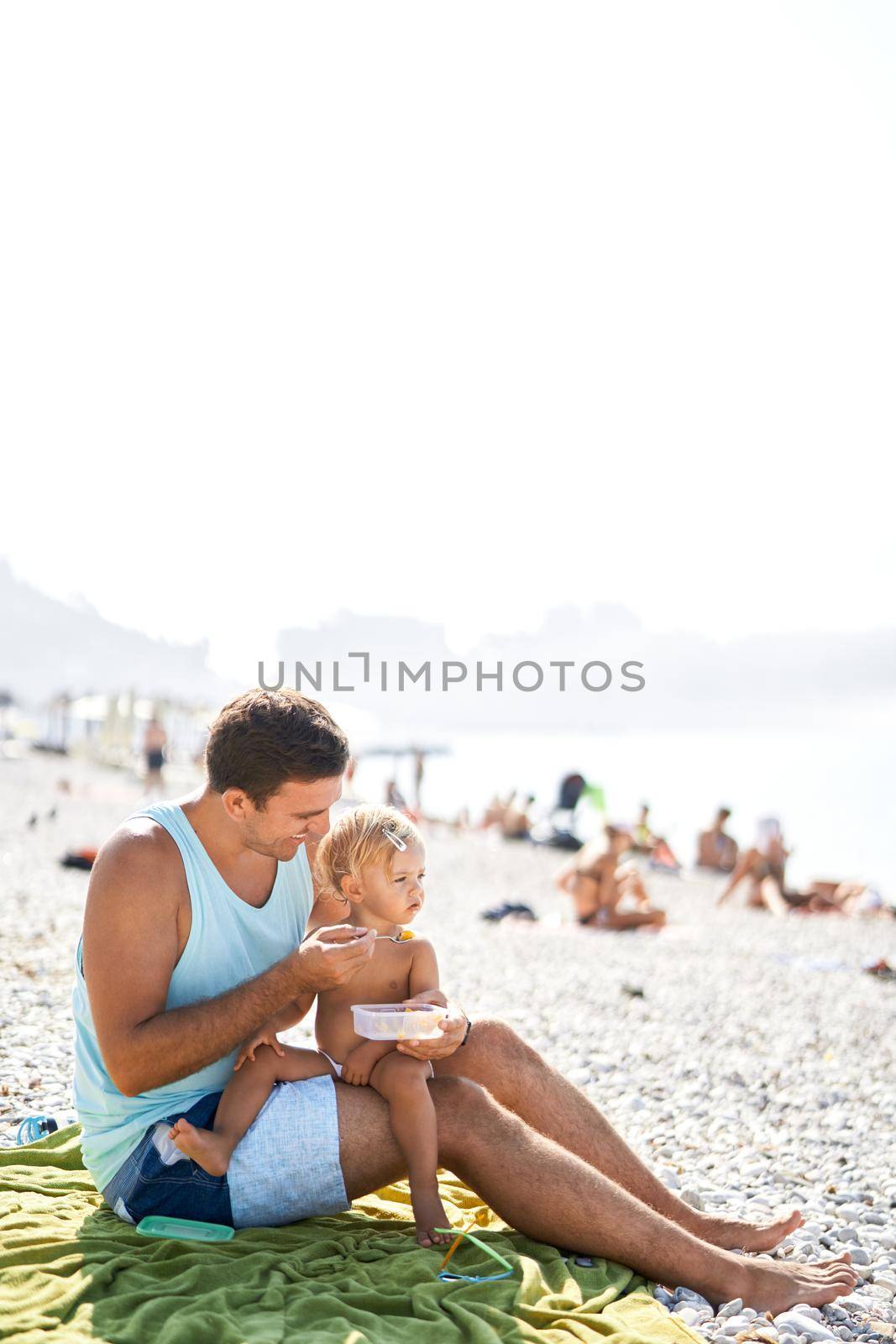 Smiling dad feeding little girl from spoon by Nadtochiy