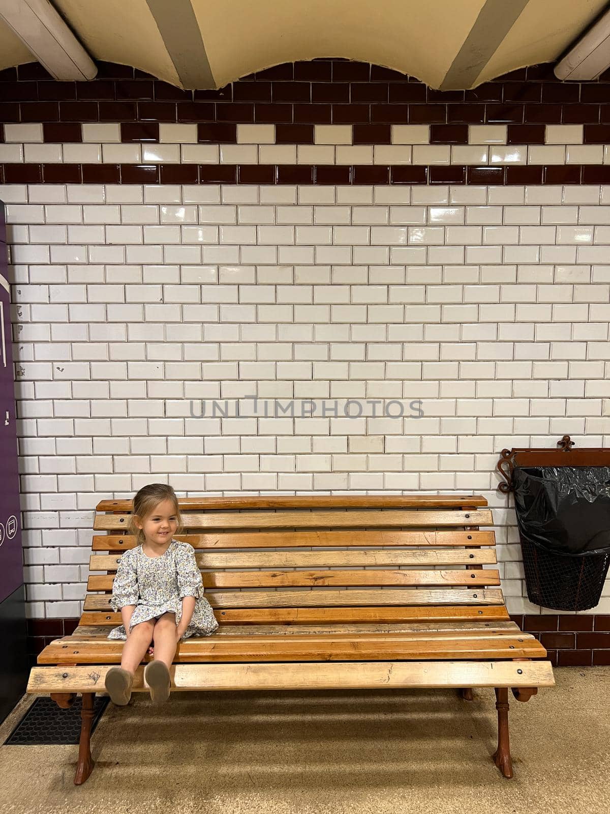 Little girl sitting on a wooden bench in the subway. High quality photo