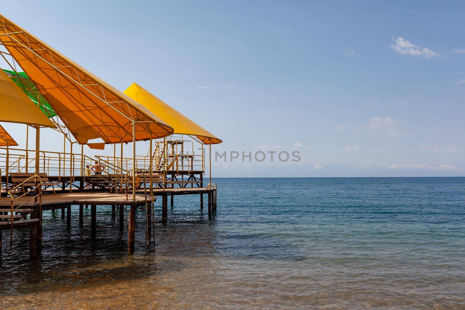 Swimming area or pier on the sea. A large pier with a roof, wooden planks and rusty stairs descending into the water. Bathing and resting place.
