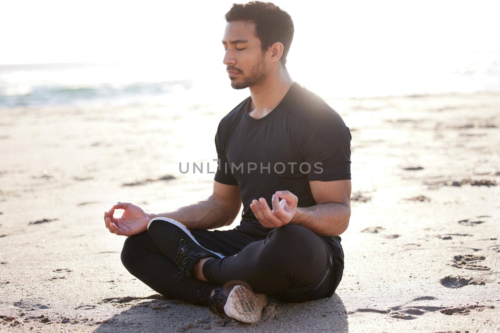 Its a matter of balance. Full length shot of a handsome young male athlete meditating on the beach