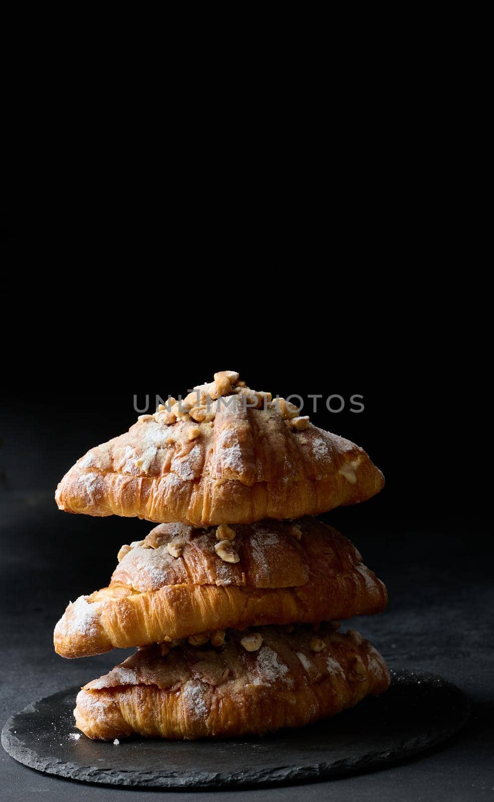 Baked croissant on a  board and sprinkled with powdered sugar, black table. Appetizing pastries for breakfast	