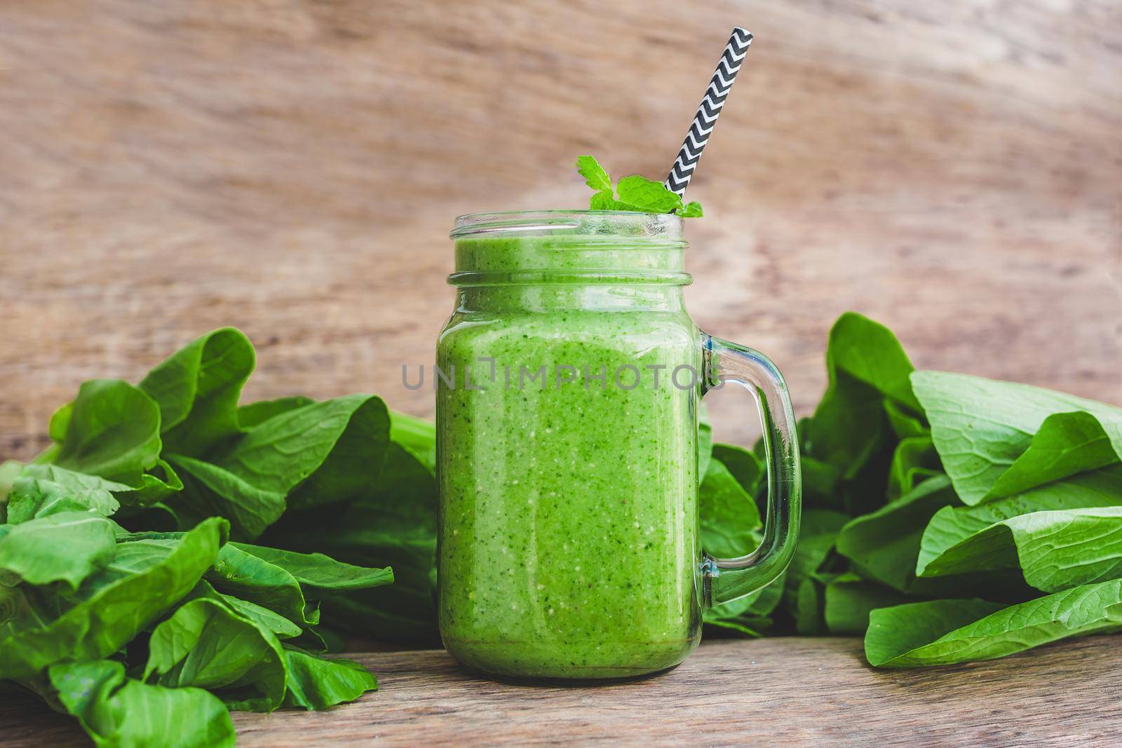 Mason jar mugs filled with green spinach, banana and coconut milk health smoothie with with a spoon of oatmeal on wooden rustic table by galitskaya