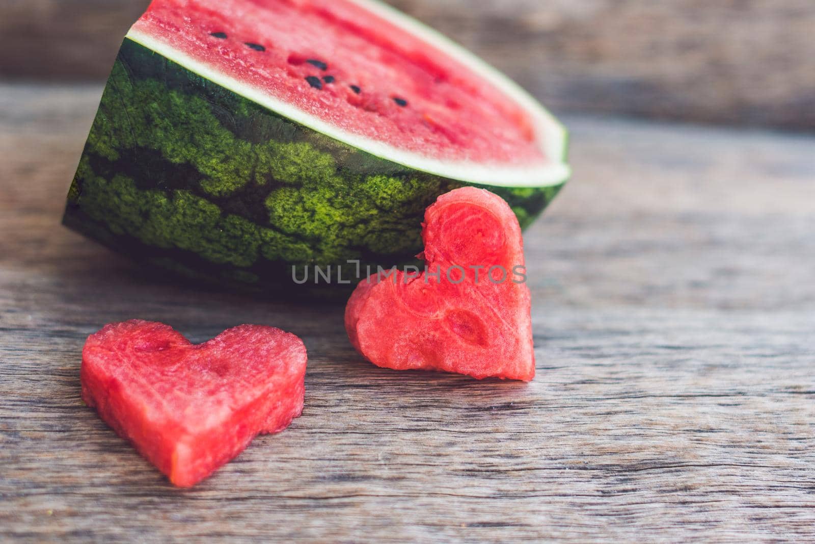 Healthy watermelon smoothie with mint, a piece of watermelon, hearts and a striped straw on a wood background.