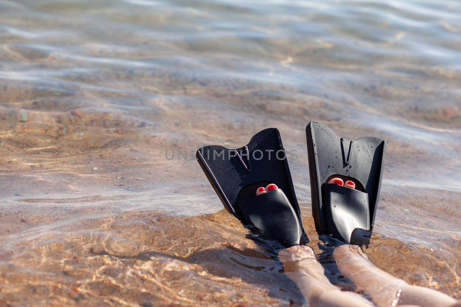 A woman in black flippers splashes near the shore. Fins stick out of the water. Swimming equipment. Summer holidays, fun, exploring the sea world concept. Space for copy.