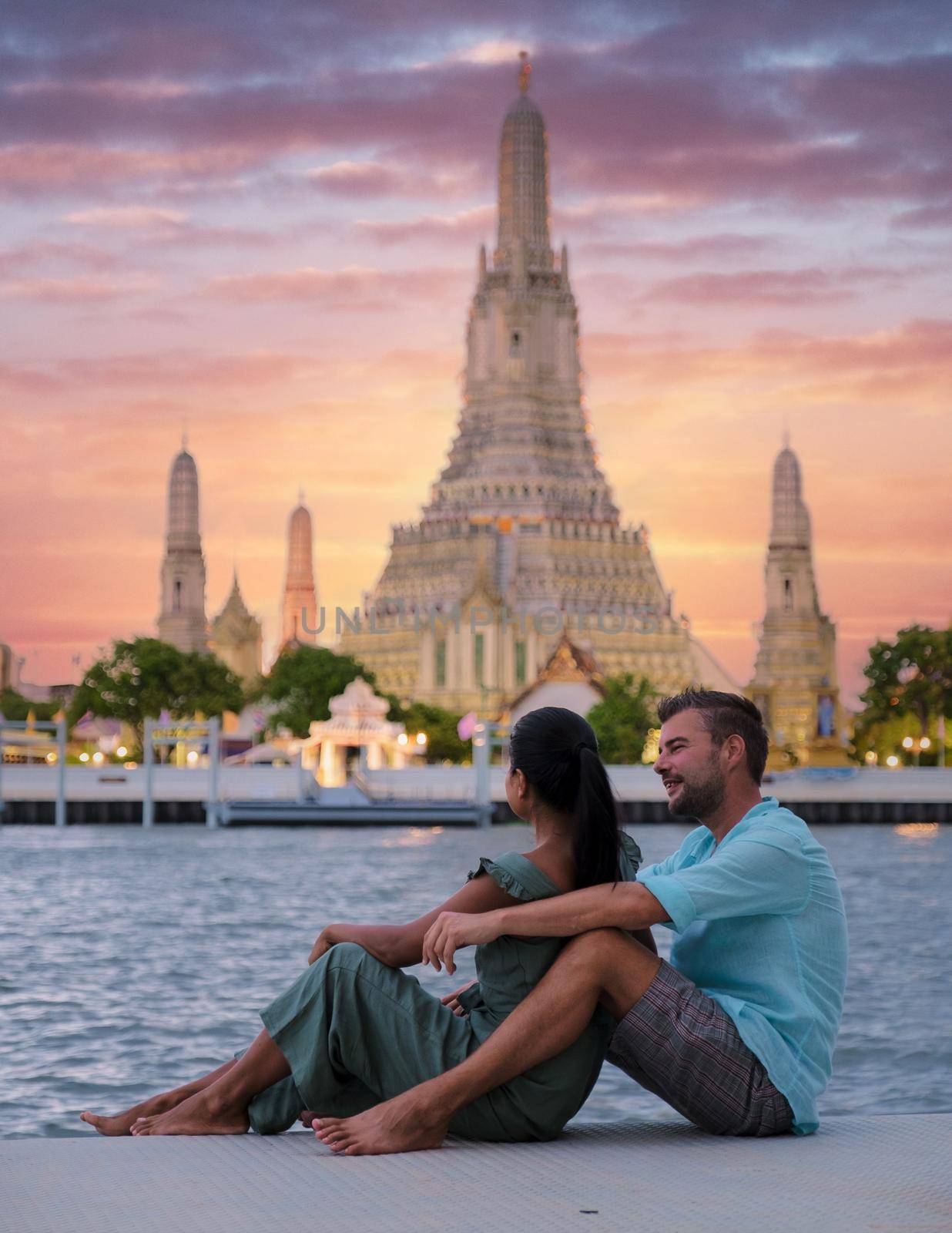Out of focus blur couple of Asian women and European men watching the sunset at Wat Arun temple in Bangkok Thailand, Temple of Dawn, Buddhist temple alongside the Chao Phraya River.