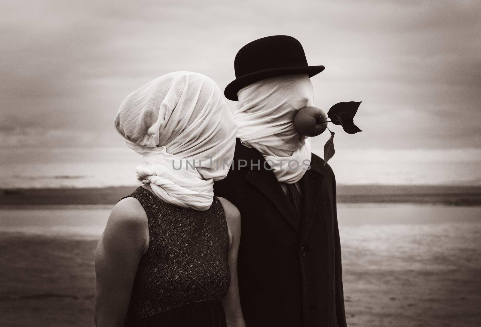 Faceless portrait of man and woman on sea background with white fabrics on their heads and green apple in a mans mouth.  Image in vintage retro style. Sepia toned and film grain added