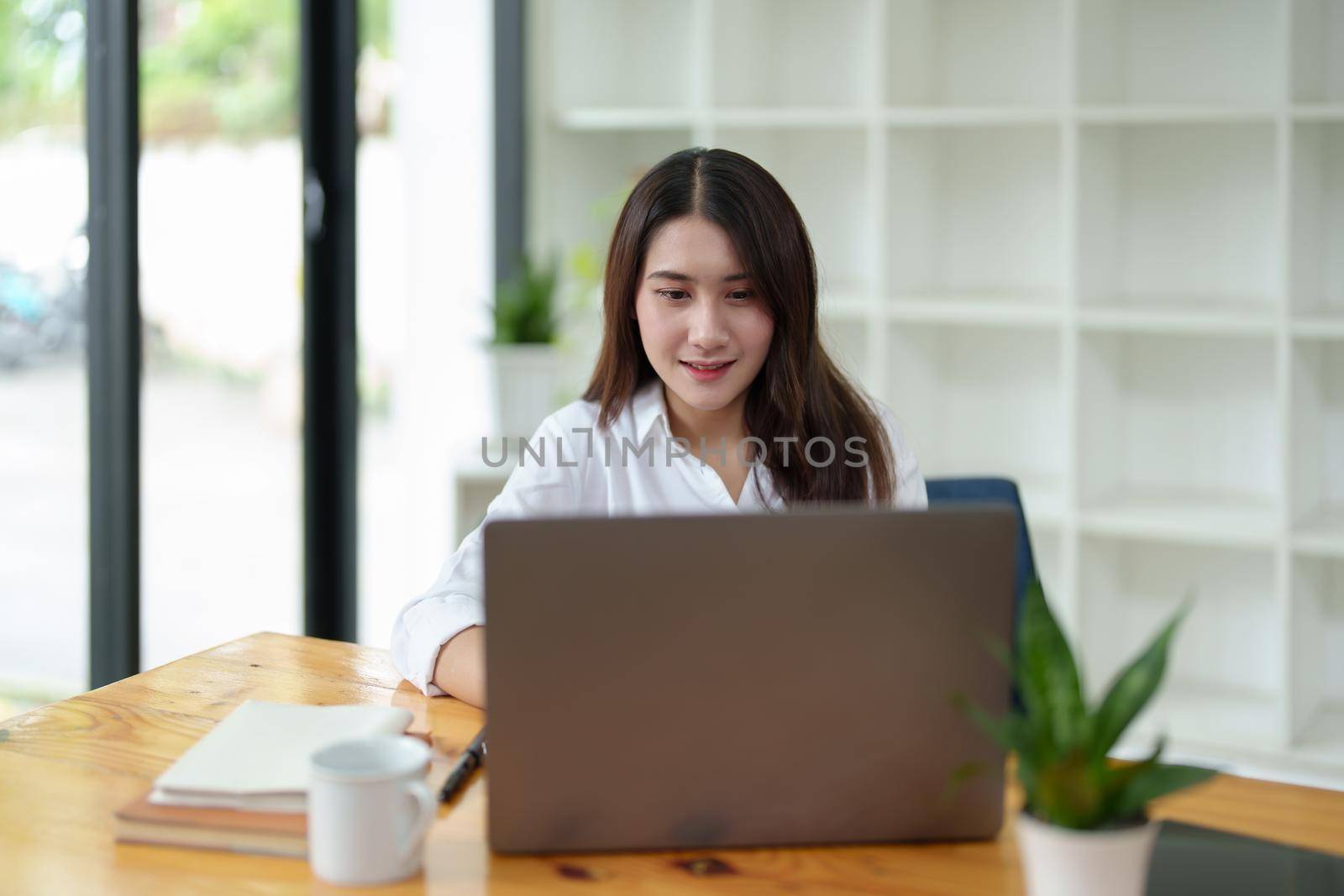 Portrait of a beautiful Asian businesswoman at work office desk with laptop computer in office by Manastrong