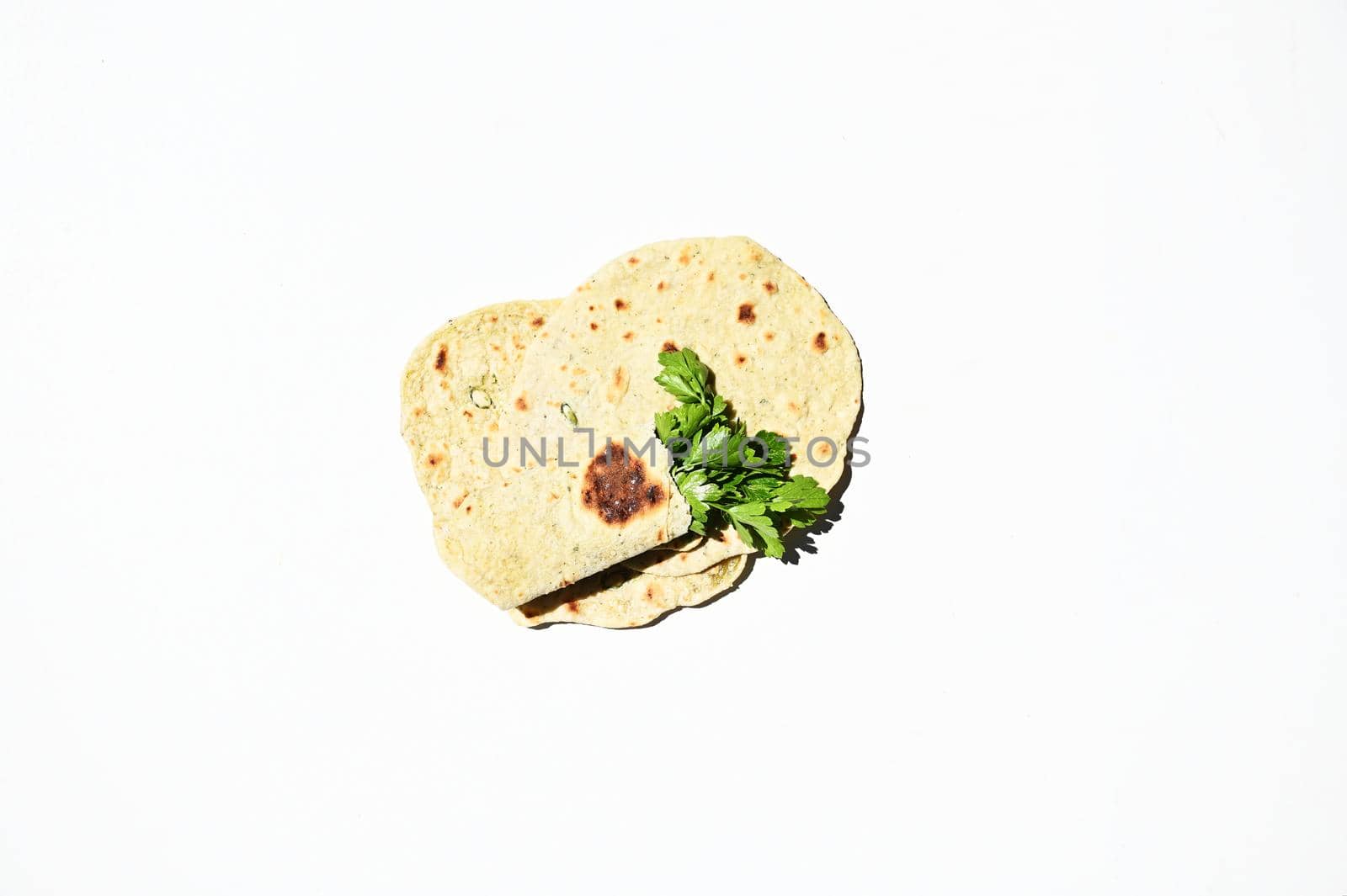 Flat lay of freshly baked homemade chapati, pita bread, flatbread with raw vegan herbs parsley, isolated on white background with copy space for advertising text. Top view, still life, food background