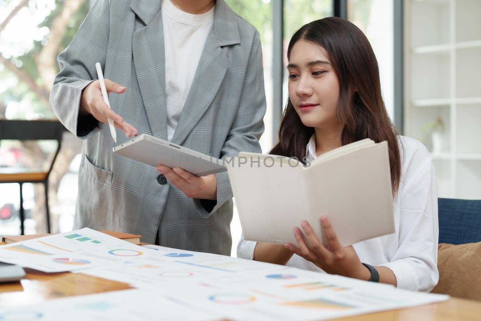 two young Asian businessusing their tablet with documents to plan marketing strategies and investments to profit from their clients by Manastrong