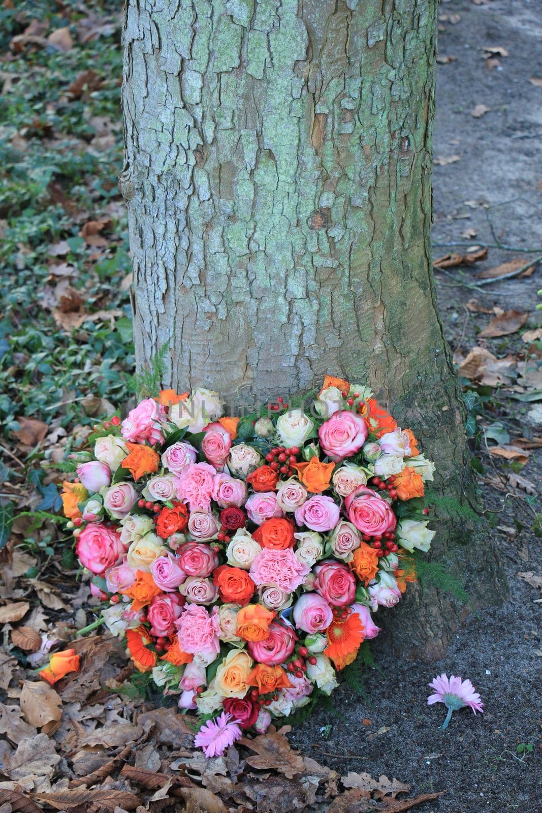 Heart Shaped sympathy or funeral flowers near a tree at a cemetery