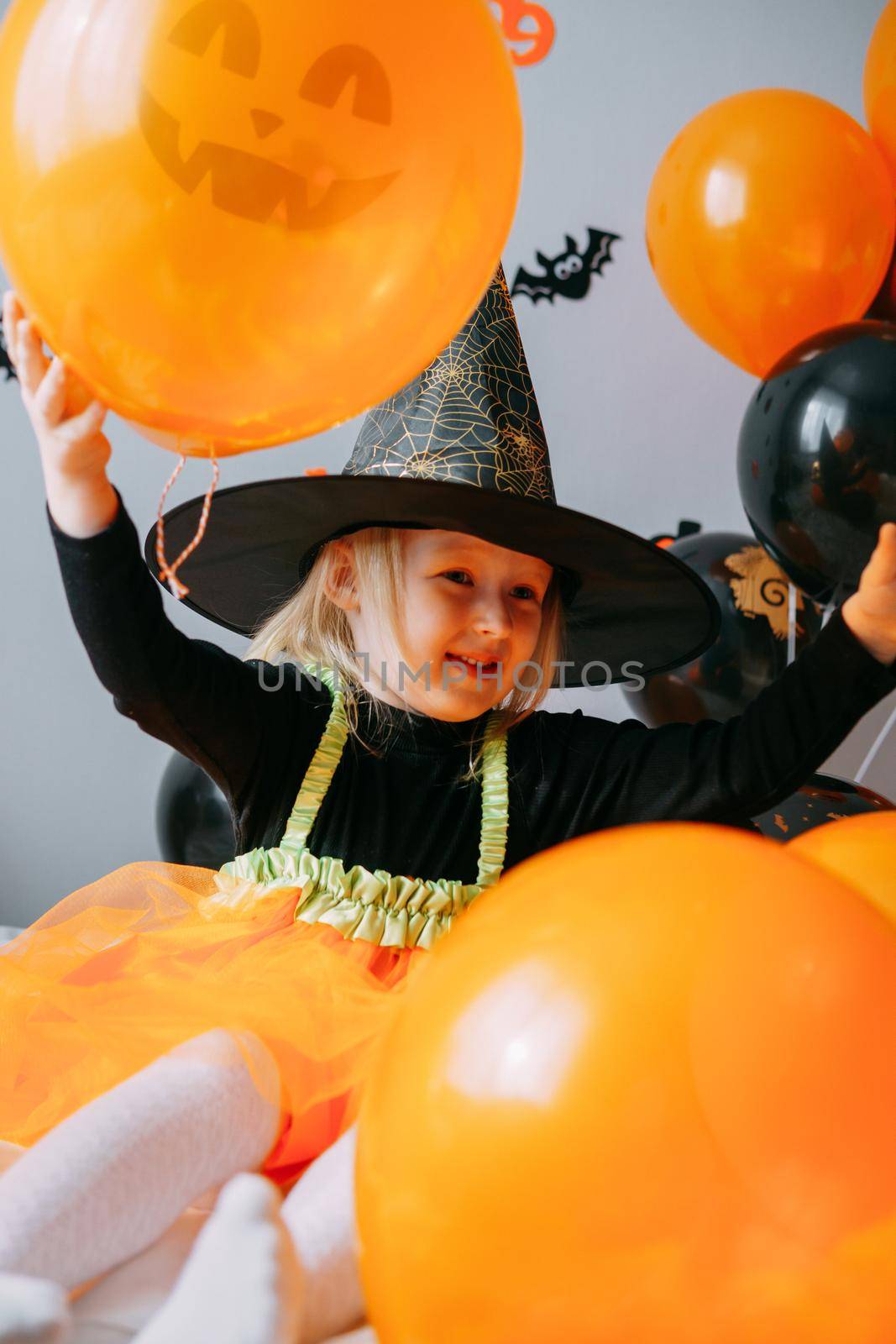 Children's Halloween - a girl in a witch hat and a carnival costume with airy orange and black balloons at home. Ready to celebrate Halloween. by Annu1tochka