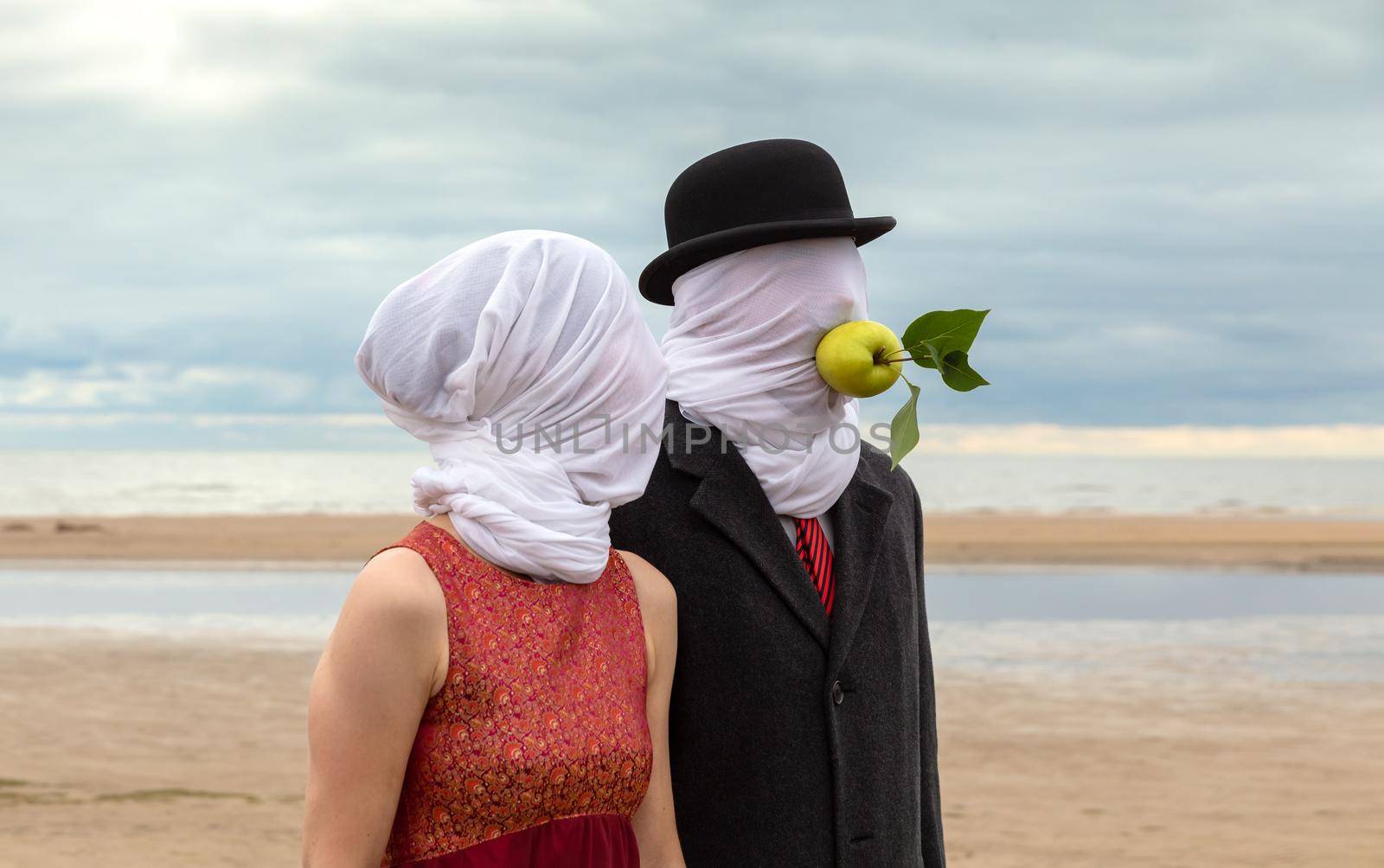 Faceless portrait of man and woman on sea background with white fabrics on their heads and green apple in a mans mouth