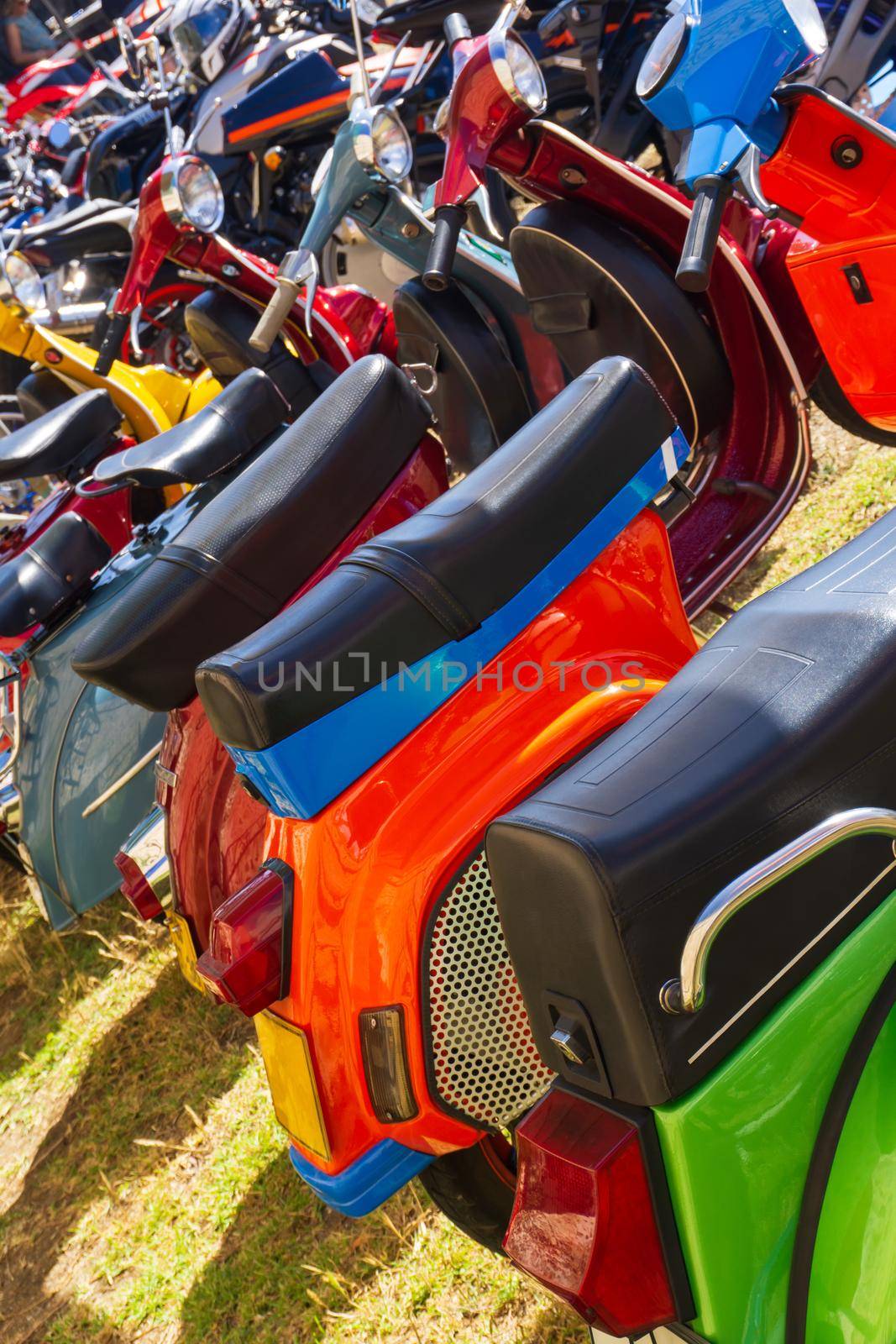 Row of brightly colored mopeds parked on the grass on a sunny day