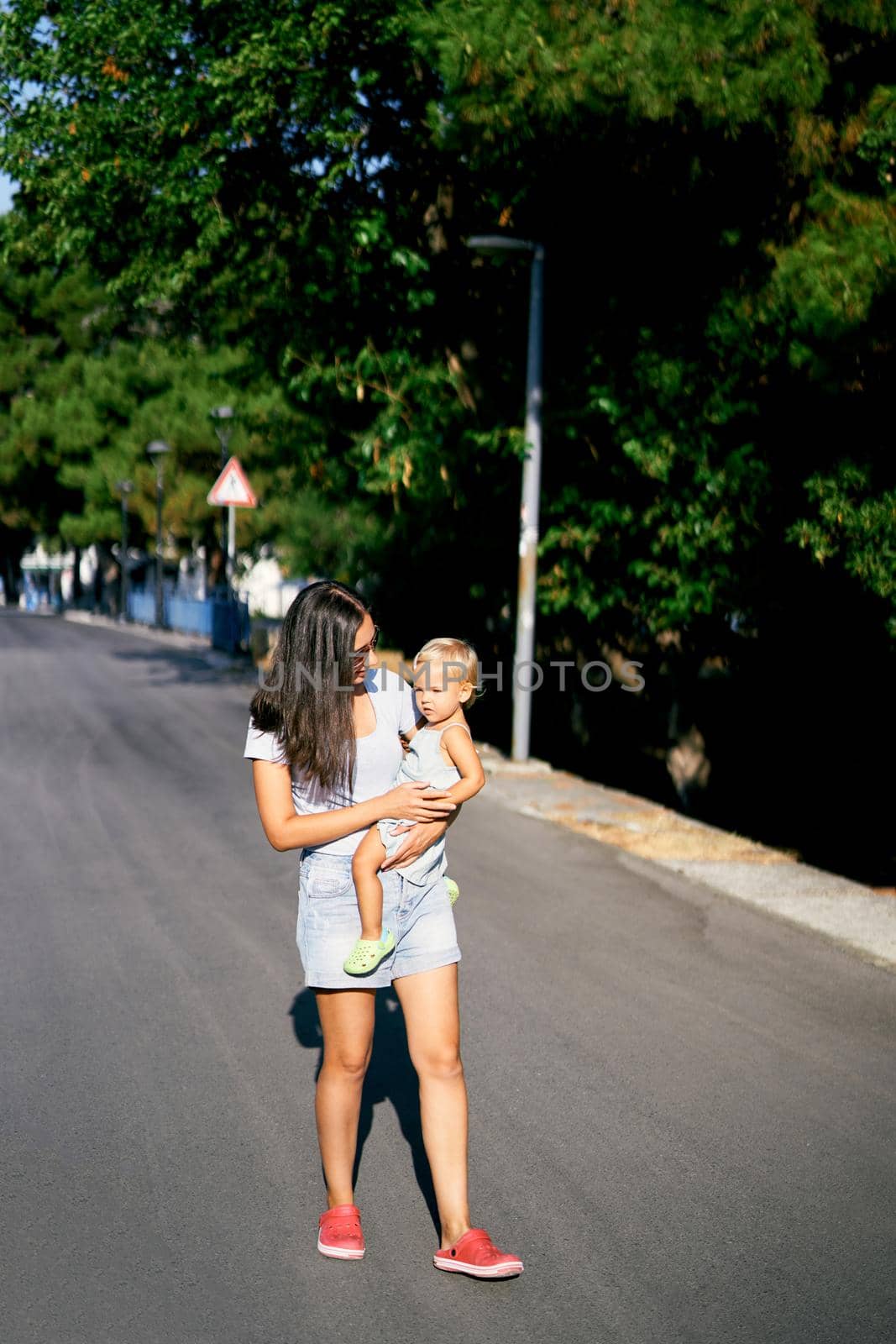 Mom carries a little girl in her arms walking along the road. High quality photo