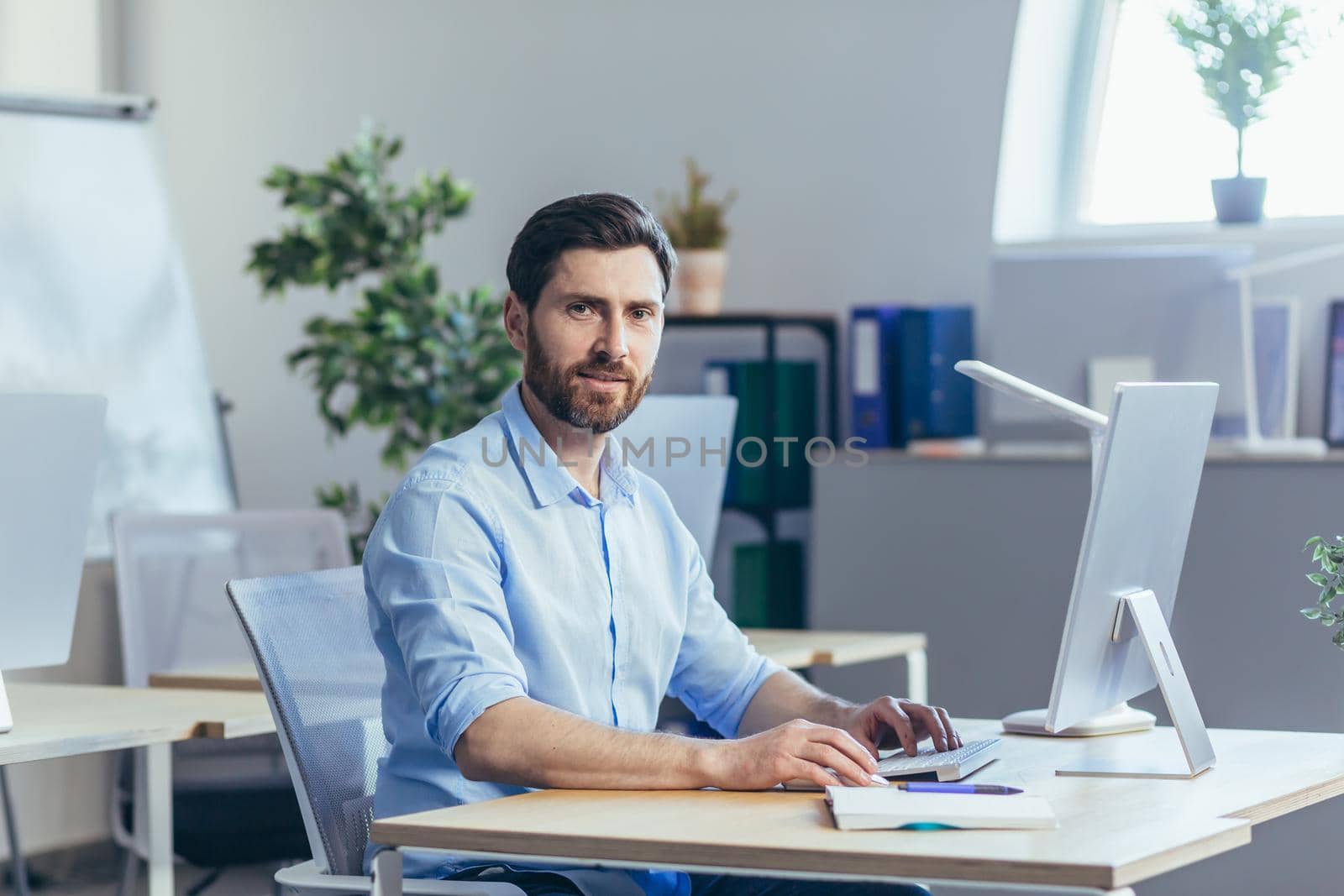 Portrait of happy worker, man working in modern bright office, looking at camera and smiling