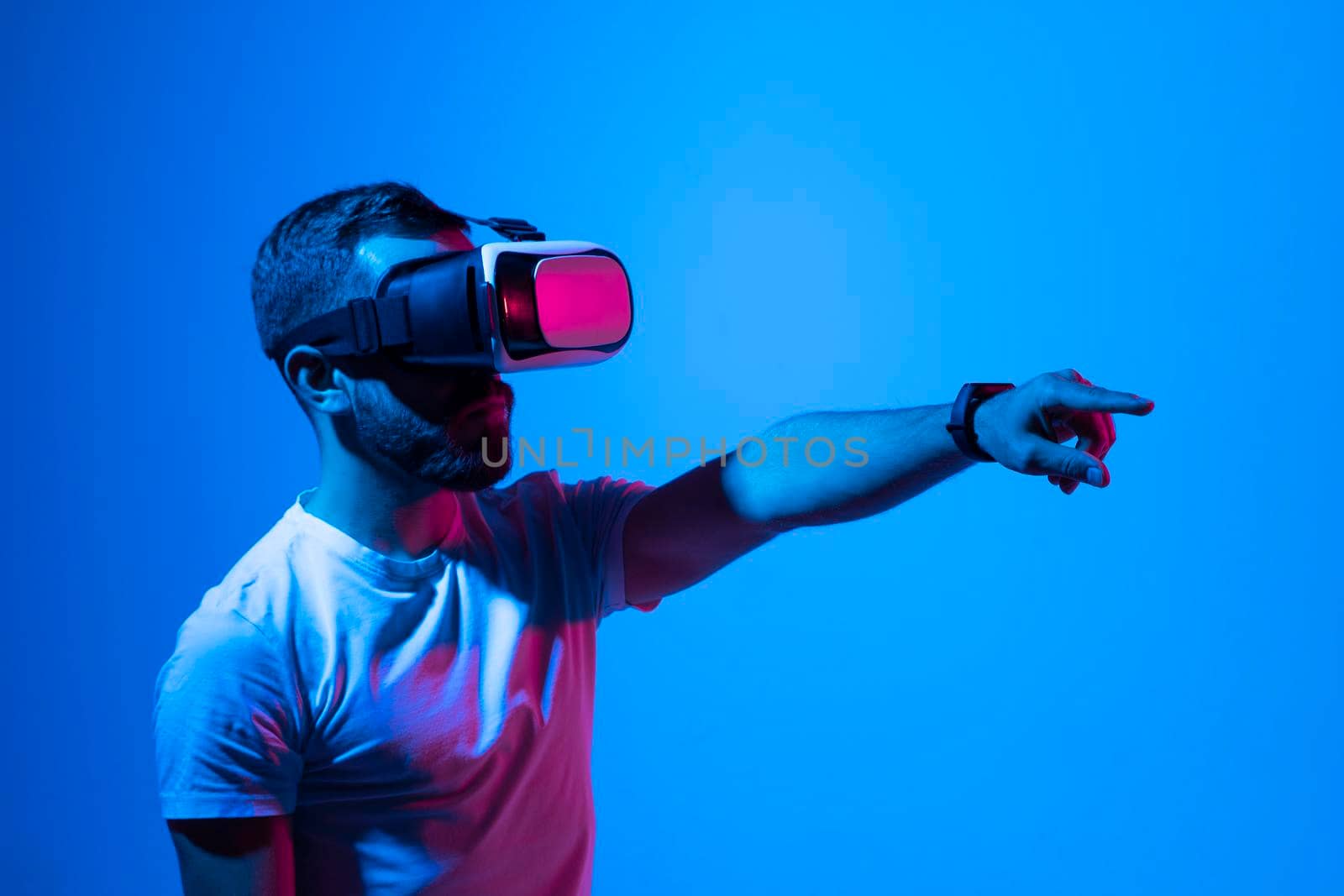 Man in white t-shirt wearing VR goggles using metaverse technology innovation in the virtual world. AR Concept over neon lighting and dark background. Virtual Reality experience. Future technology