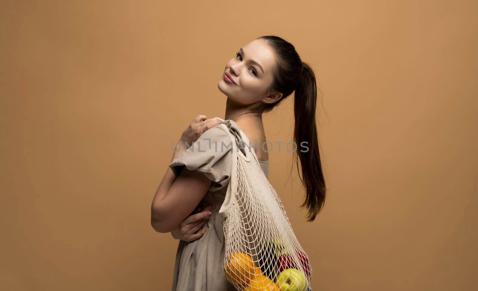 Young brunette woman with cotton reusable mesh bag full of fruits. Shopping without plastic packaging in plastic free grocery store