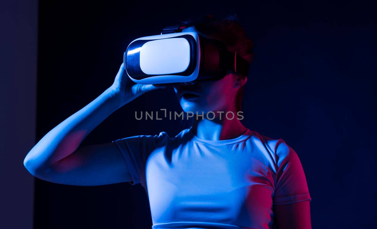 Young woman using VR goggles in colorful neon lights and having fun playing a games with a friends. Wearable virtual augmented reality