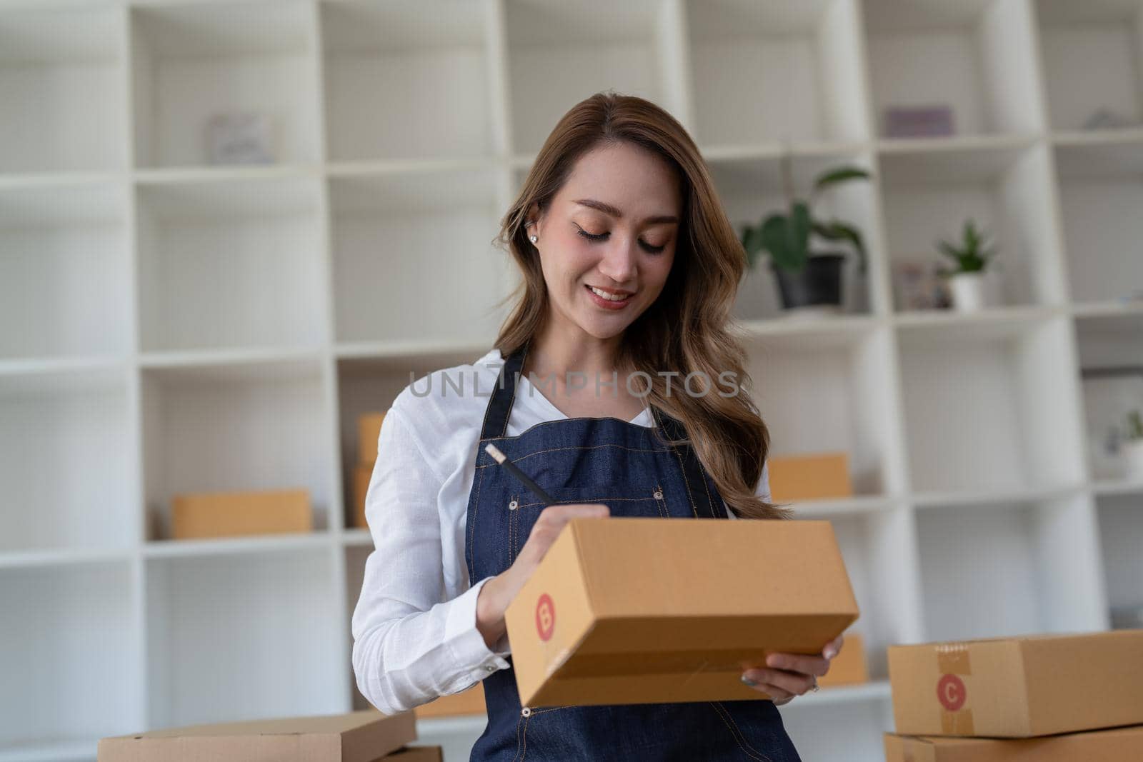 Portrait young attractive asia female owner startup business look at camera work happy with box at home prepare parcel delivery in sme supply chain, procurement, omnichannel commerce online concept