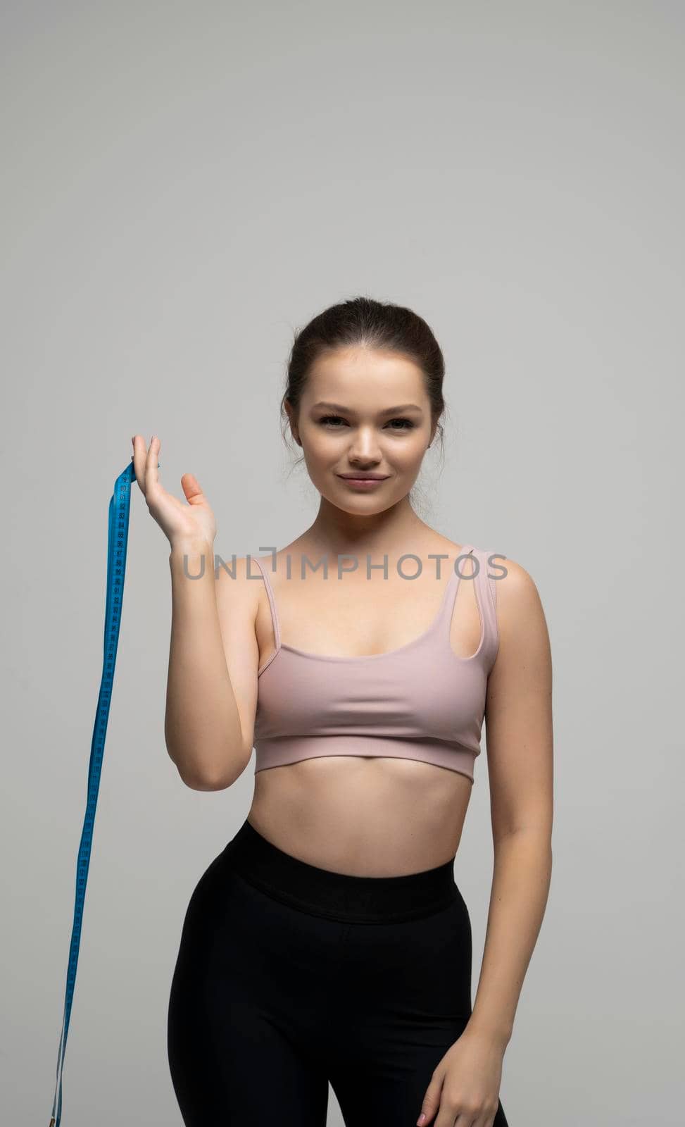 Young brunette woman in fitness outfit holding a blue measure tape and looking in a camera