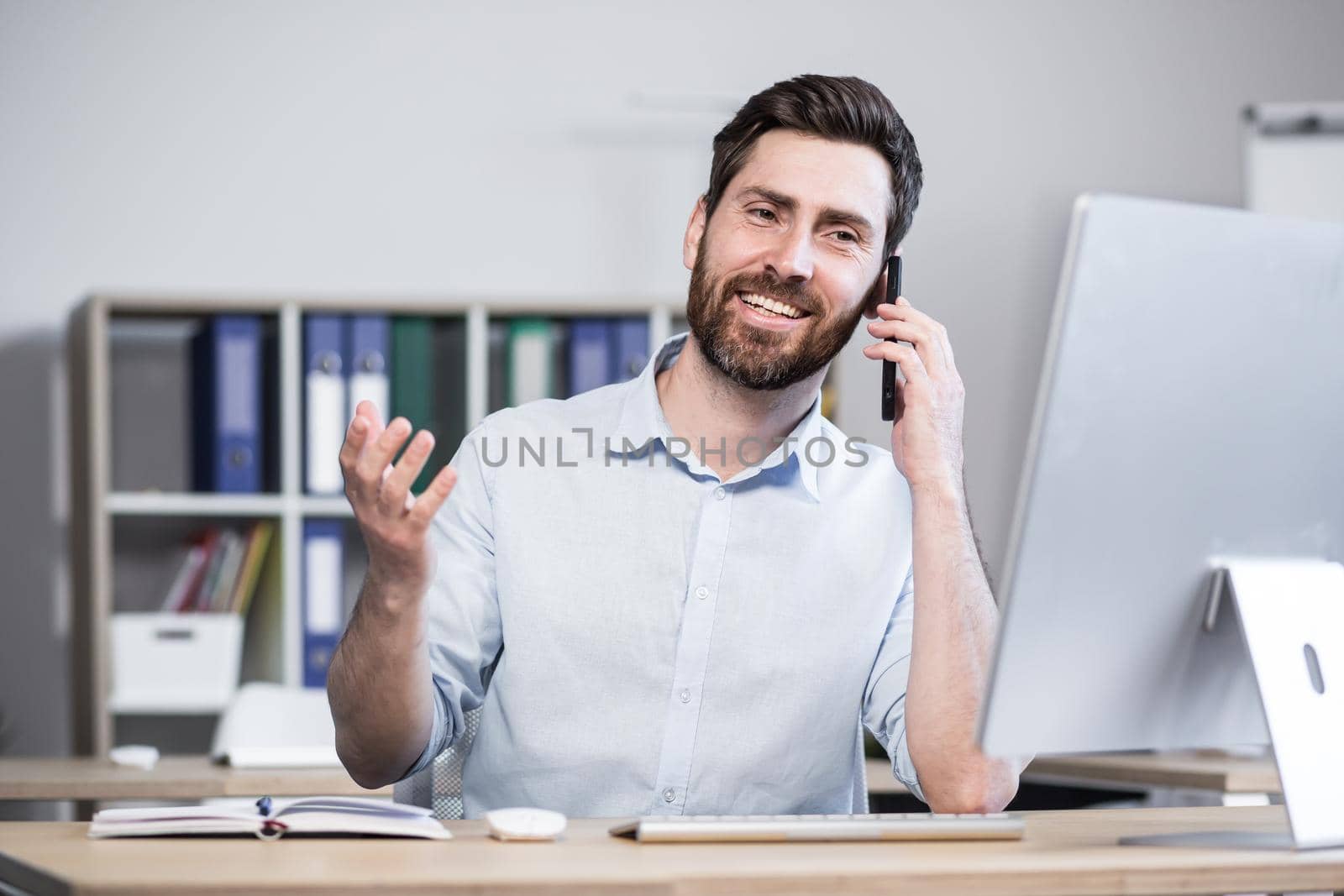 Successful male programmer working in the office at the computer talking to colleagues on the phone smiling.