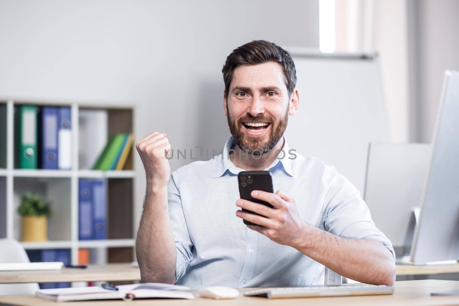 Happy businessman reading good news from the phone, man working in the office