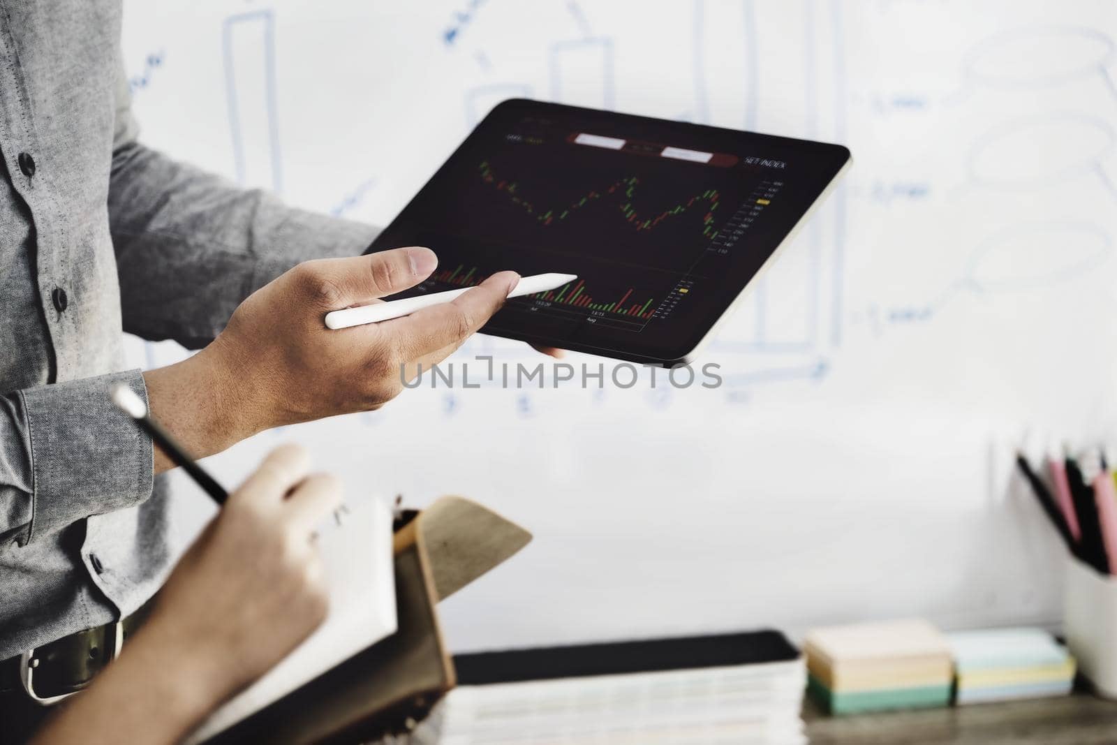 An investment expert points a pen at a tablet monitor to analyze the stock market to teach you how to make a profit. by Manastrong