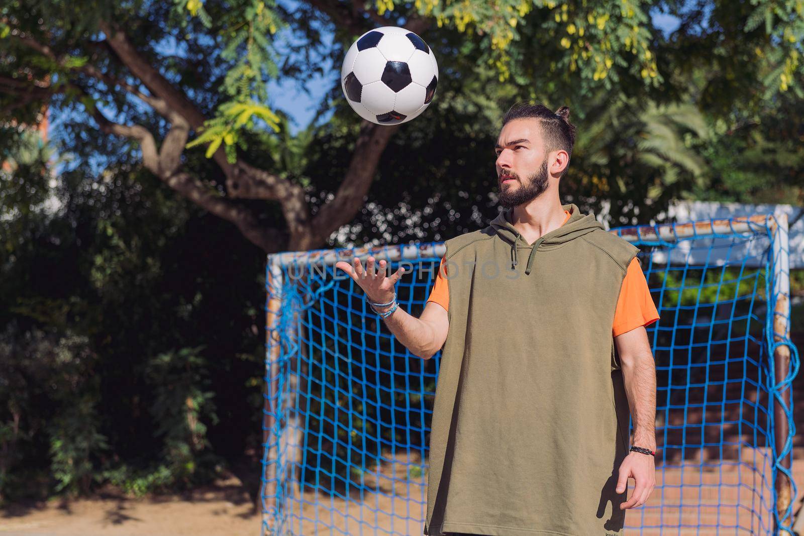 handsome hipster football player in front of the goal of an urban court throwing the ball with the hand, concept of healthy lifestyle and urban sport in the city, copy space for text
