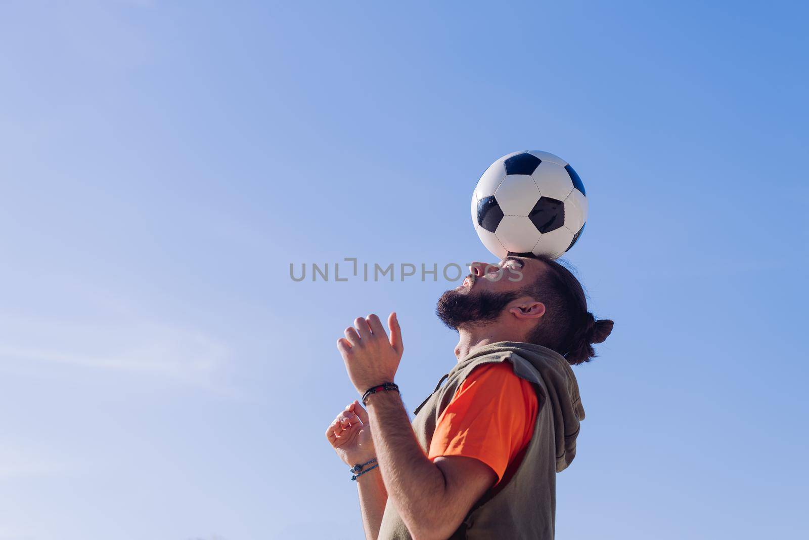 portrait of a football player playing balancing the ball on his head with a clear blue sky in the background, concept of healthy lifestyle and urban sport in the city, copy space for text