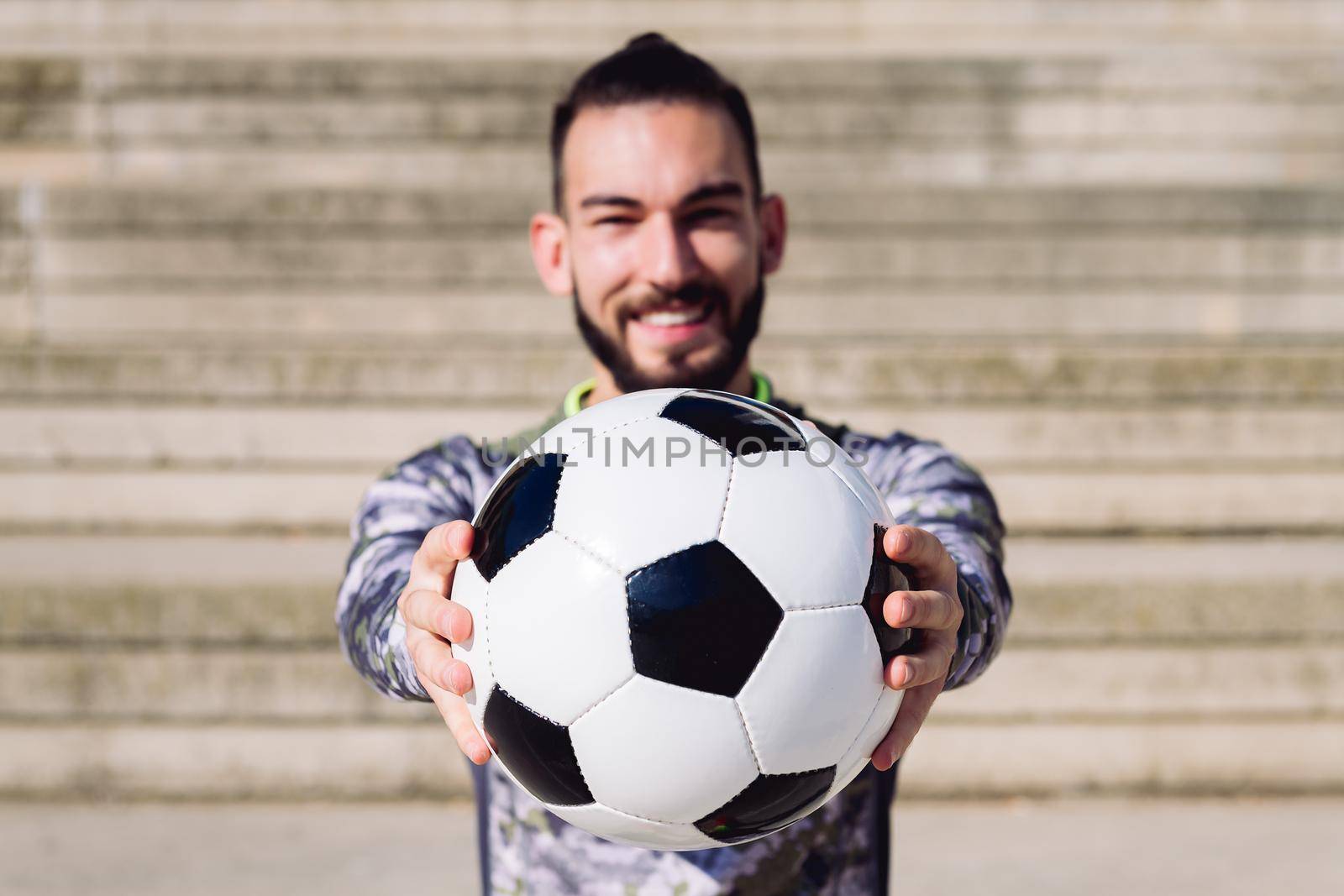 football ball in the hands of a smiling sportsman in a concrete soccer court, selective focus on the ball, concept of healthy lifestyle and urban sport in the city, copy space for text