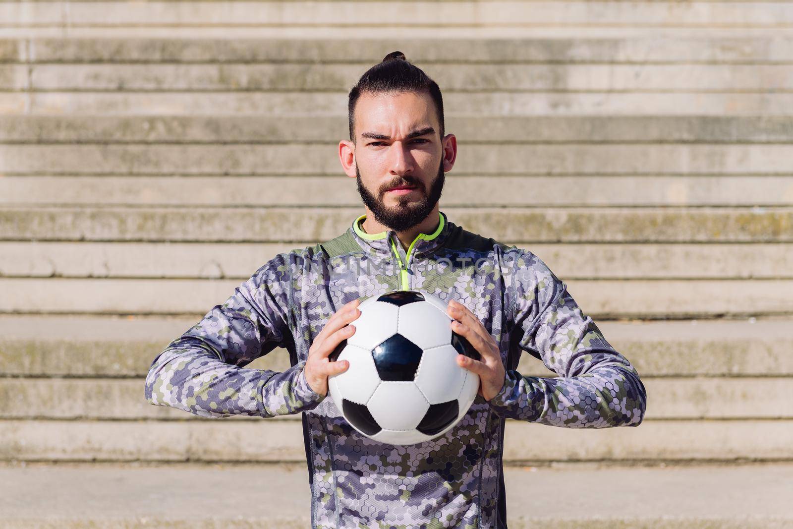 horizontal portrait of an attractive hipster sportsman in a concrete soccer court with the football ball in his hands, concept of healthy lifestyle and urban sport in the city, copy space for text