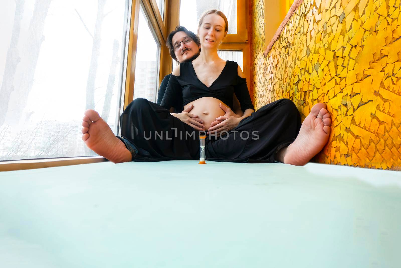 pregnancy, love, family and people concept - pregnant woman and her husband making hand heart gesture on her belly sitting in the lotus position. High quality photo