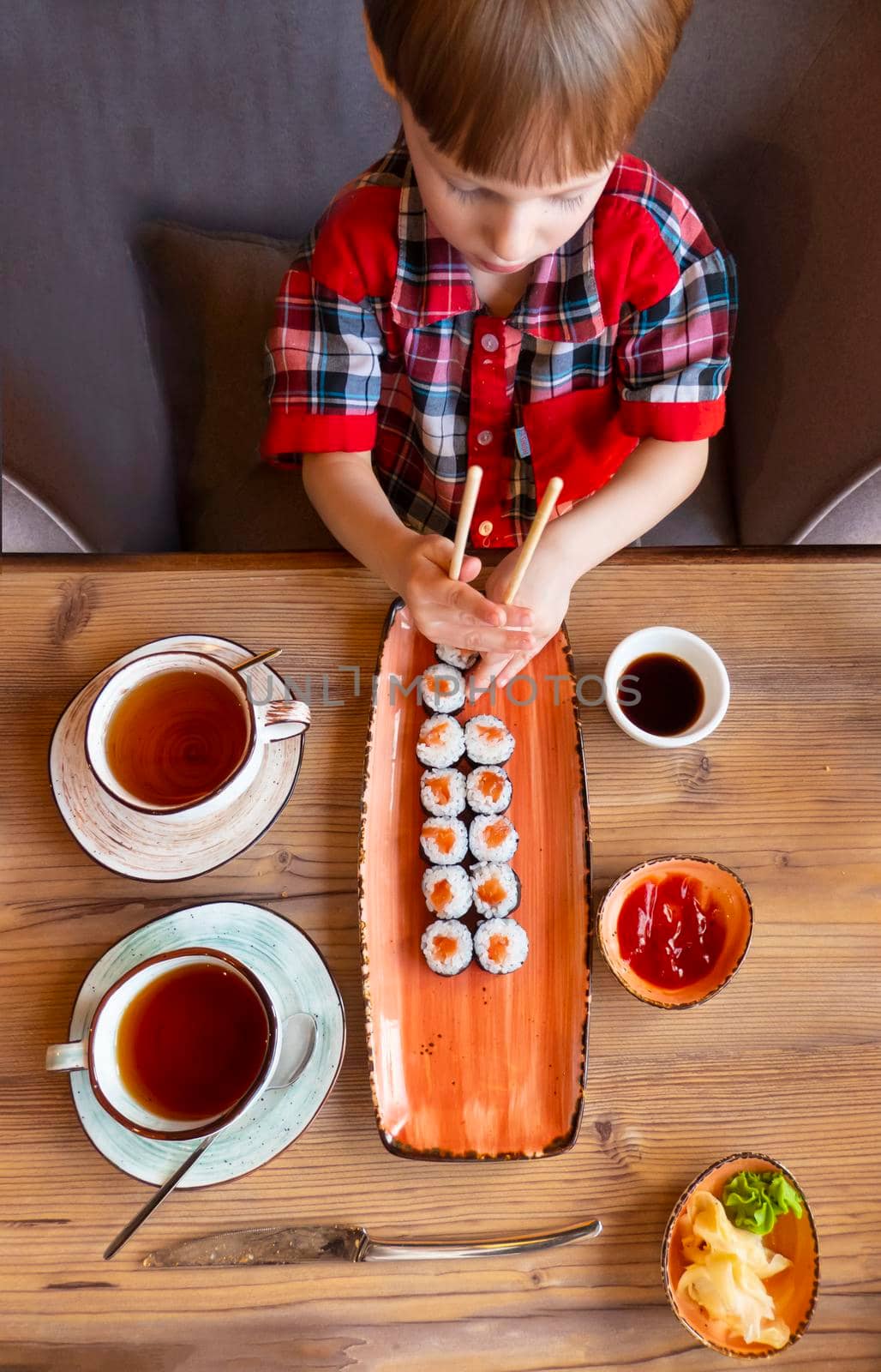 Little cute little boy eating sushi in a cafe, concept of eating. the boy in the restaurant eats sushi, dumbly holding chopsticks. View from aboveHigh quality photo