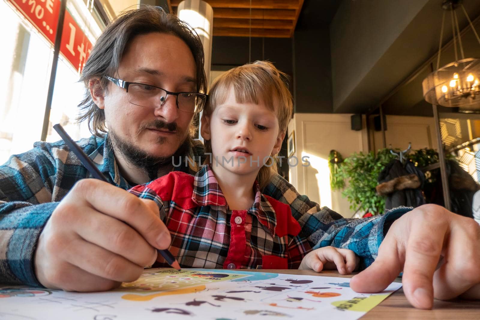 a child with his father in a restaurant draws a coloring book, waiting for cooking