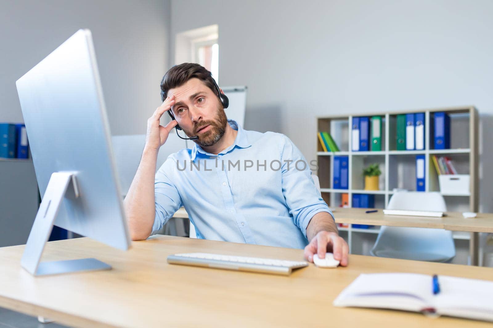 Upset businessman with headset working in office with computer