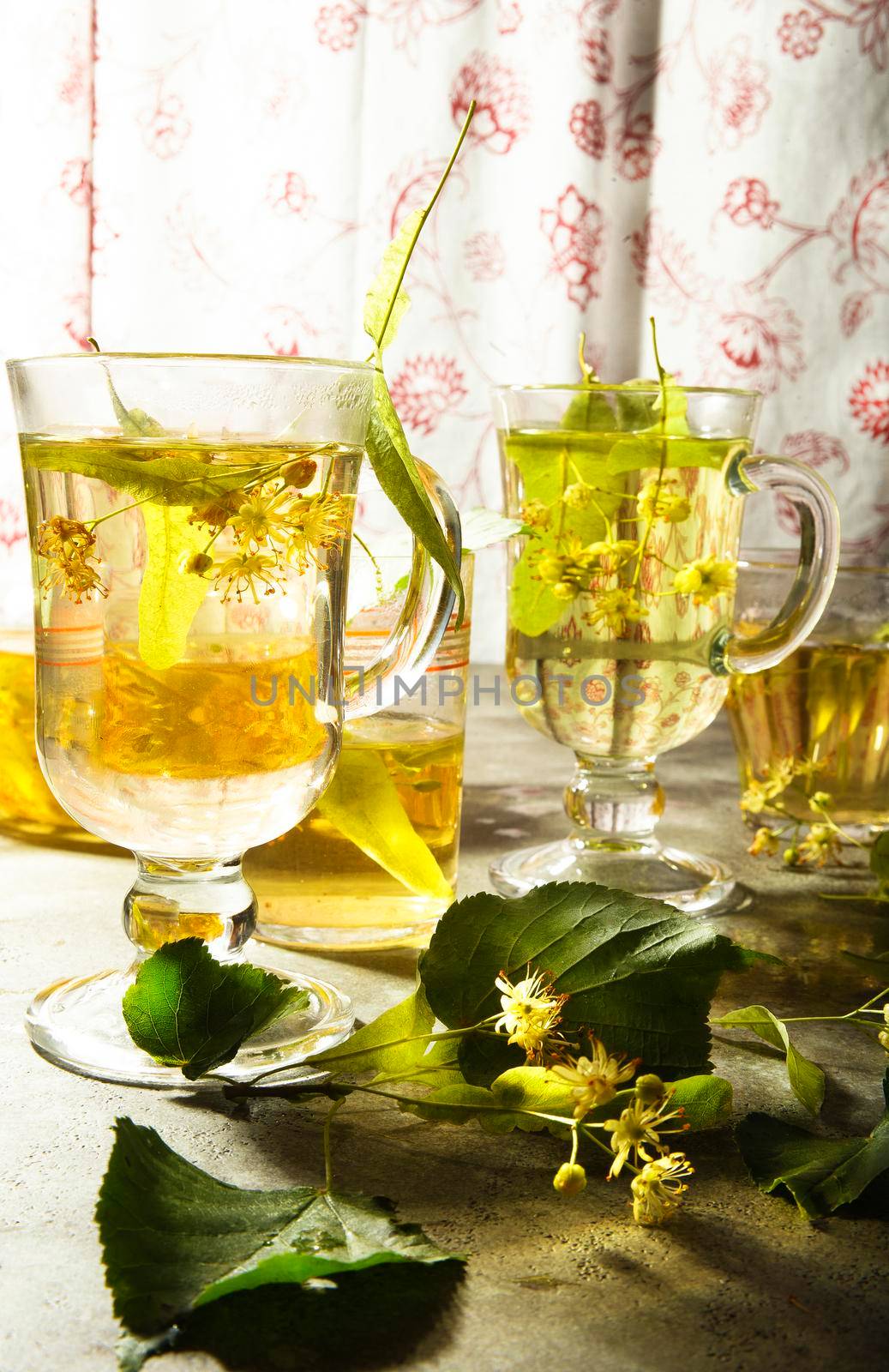 Two glass cups of freshly made yellow linden tea with leaves and flowers of linden tree, selective focus.