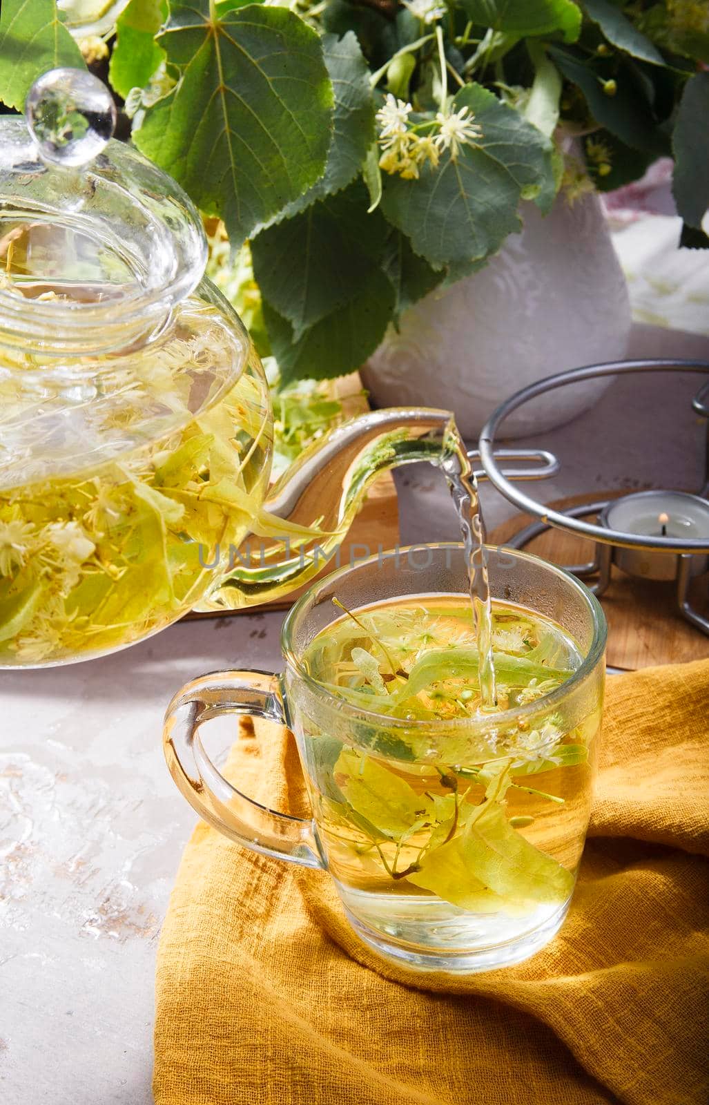 A teapot and a glass cup of freshly made linden tea on white table, selective focus