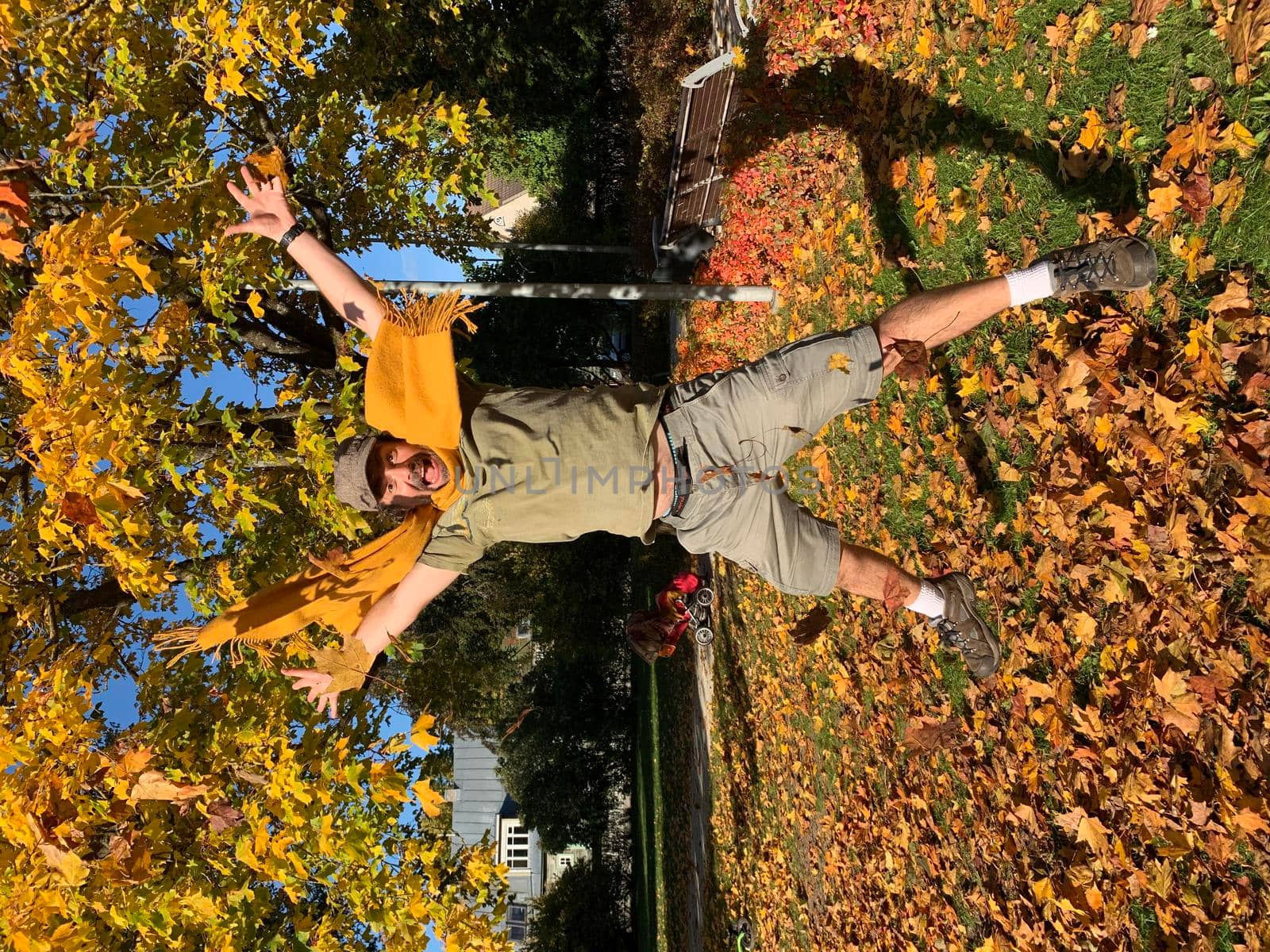 Mature man in yellow scarf jumping in autumn park by Varaksina