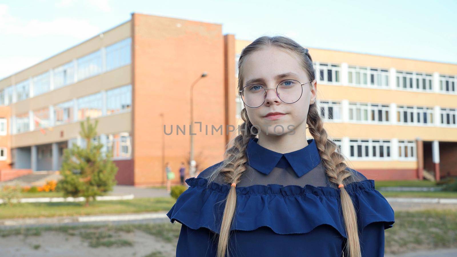 A teenage girl wearing glasses in front of a school