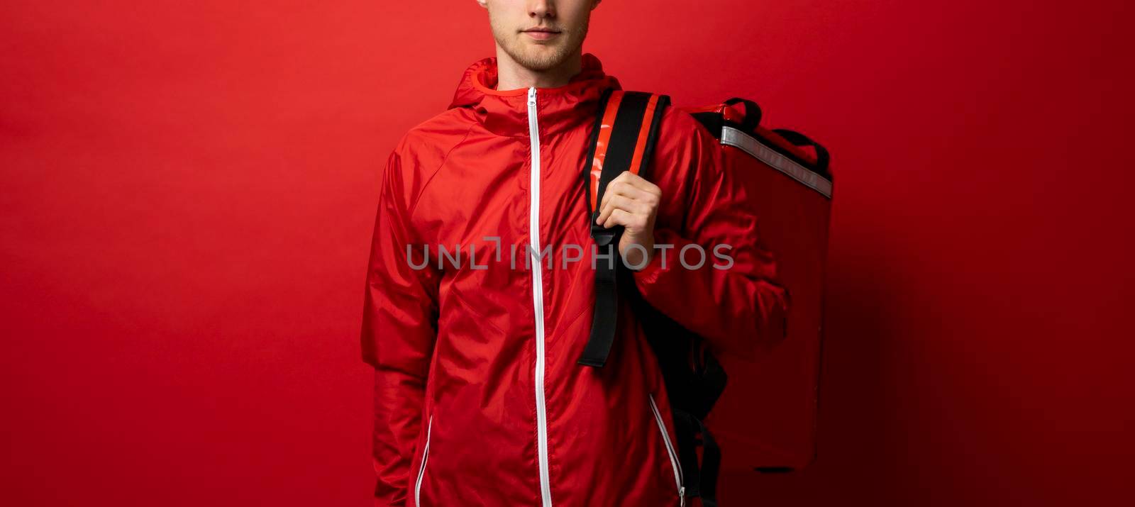 Delivery guy employee man in red uniform workwear work as dealer courier hold red thermal food bag backpack isolated on red color background studio. Service concept. by vovsht