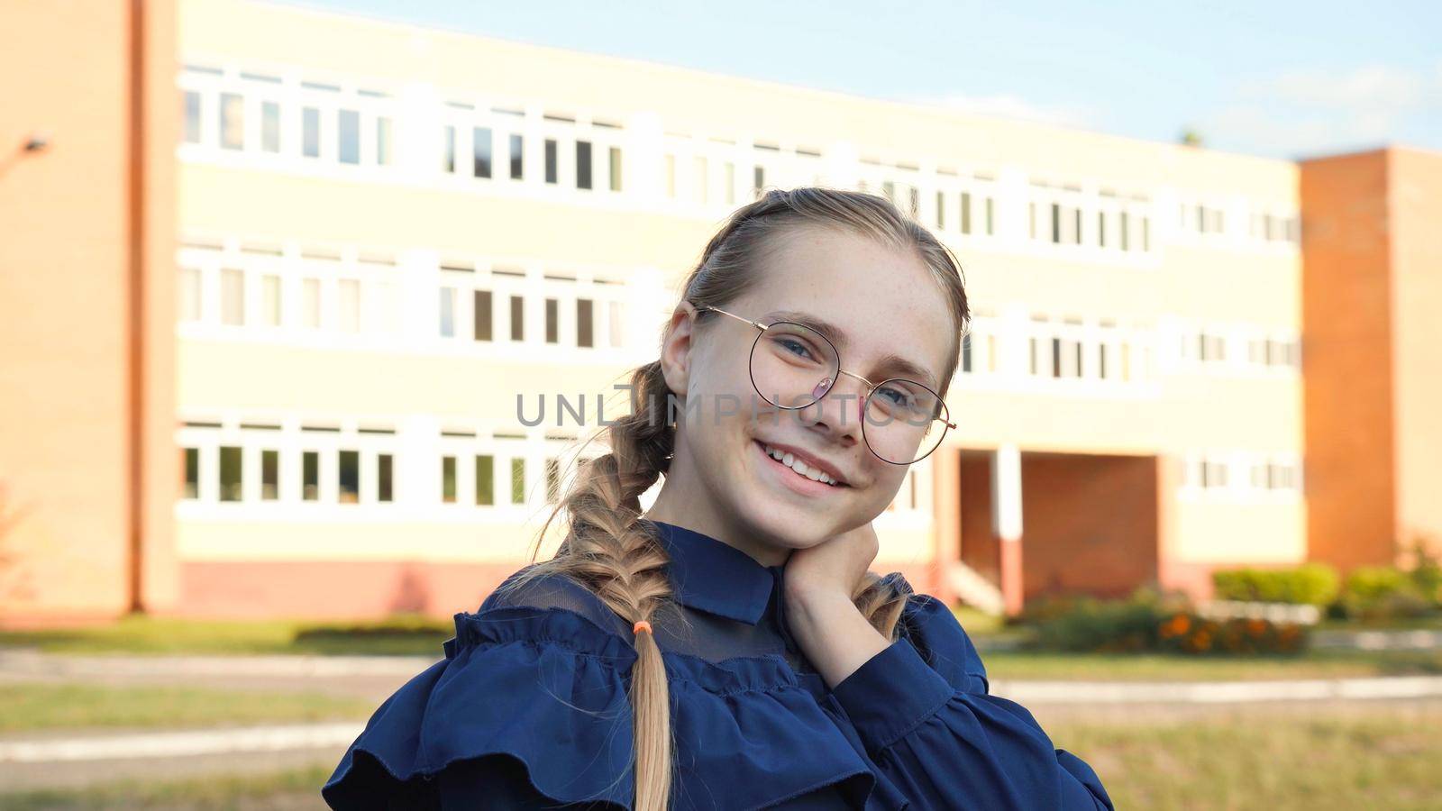 A teenage girl wearing glasses in front of a school