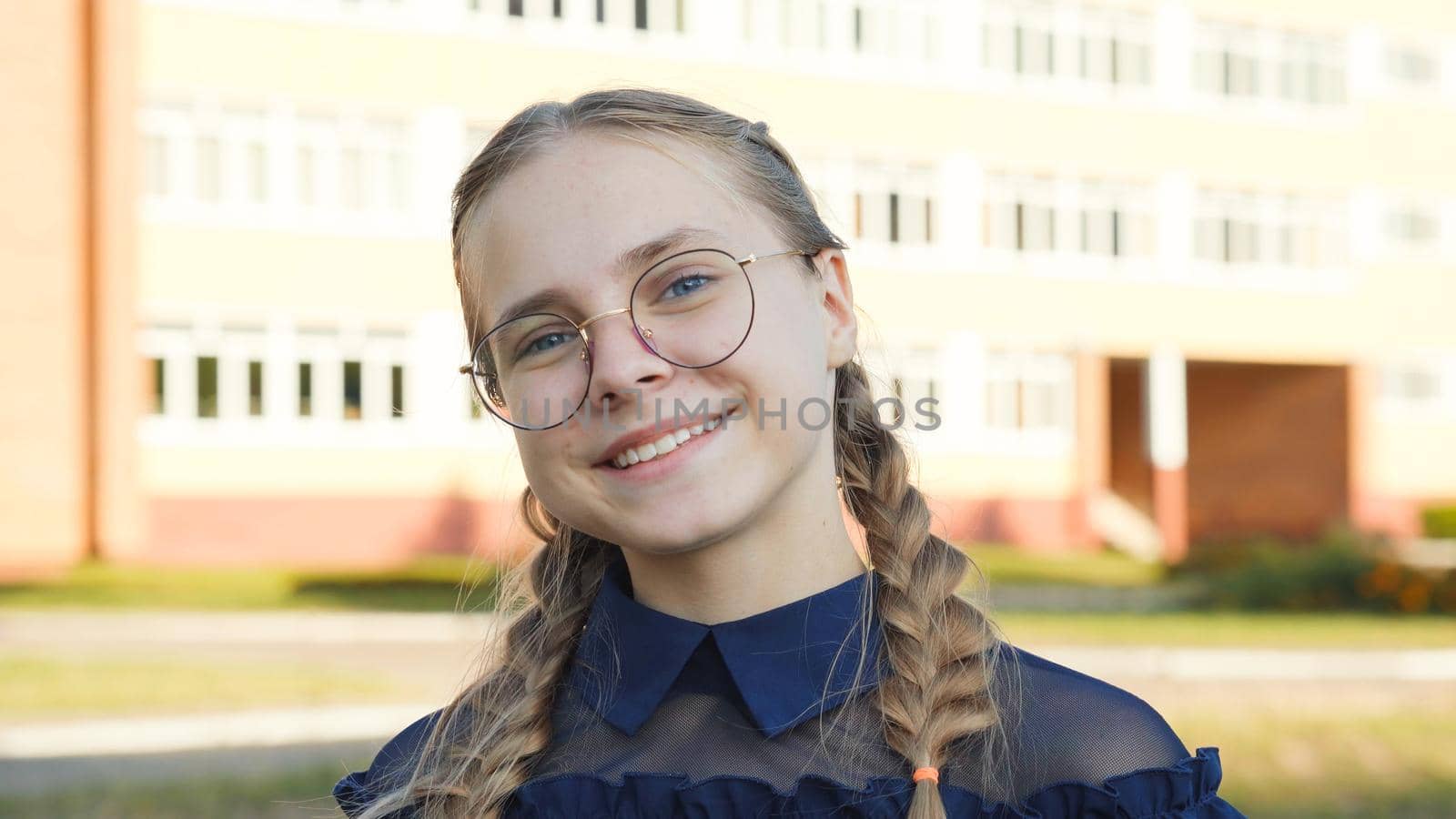 A teenage girl wearing glasses in front of a school