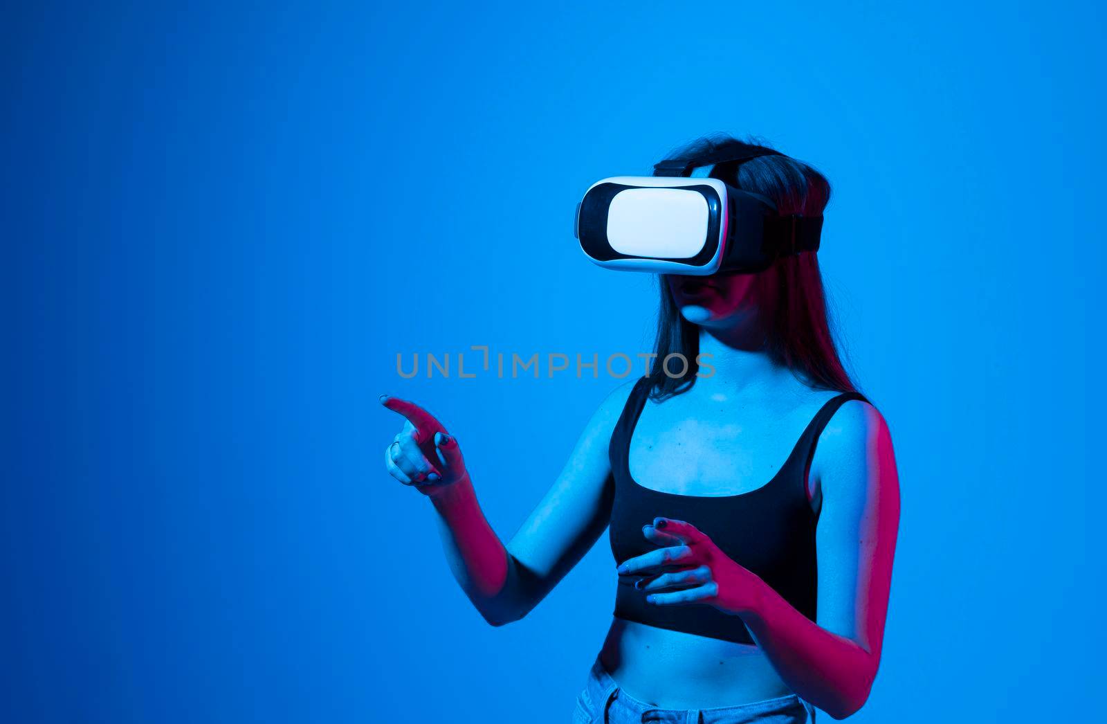 Young woman using virtual reality headset in neon light. VR, future, gadgets, metaverse, technology, education online, studying, video game concept