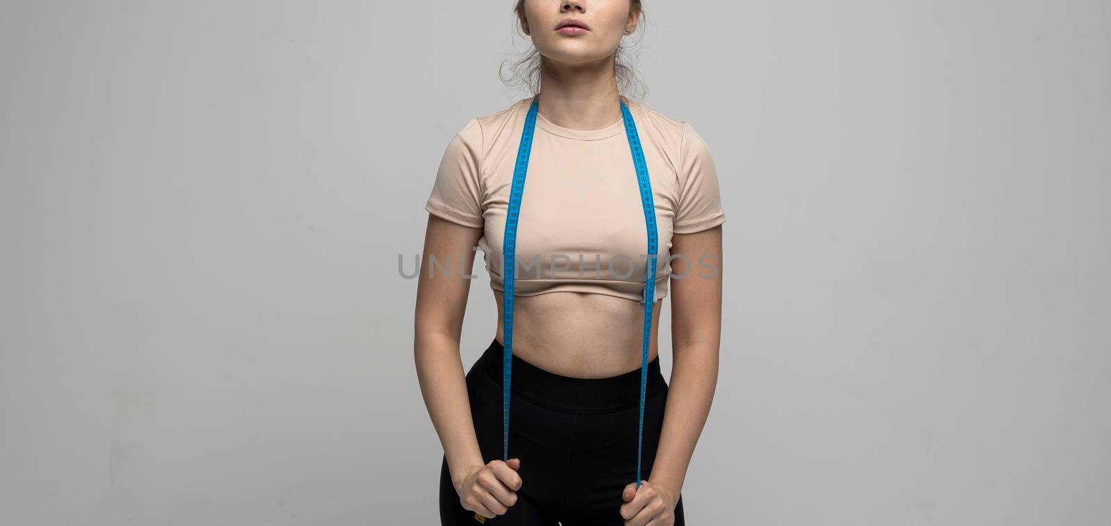 Crop image of attractive brunette woman in sportswear with blue measuring tape around her neck. Sports and diets